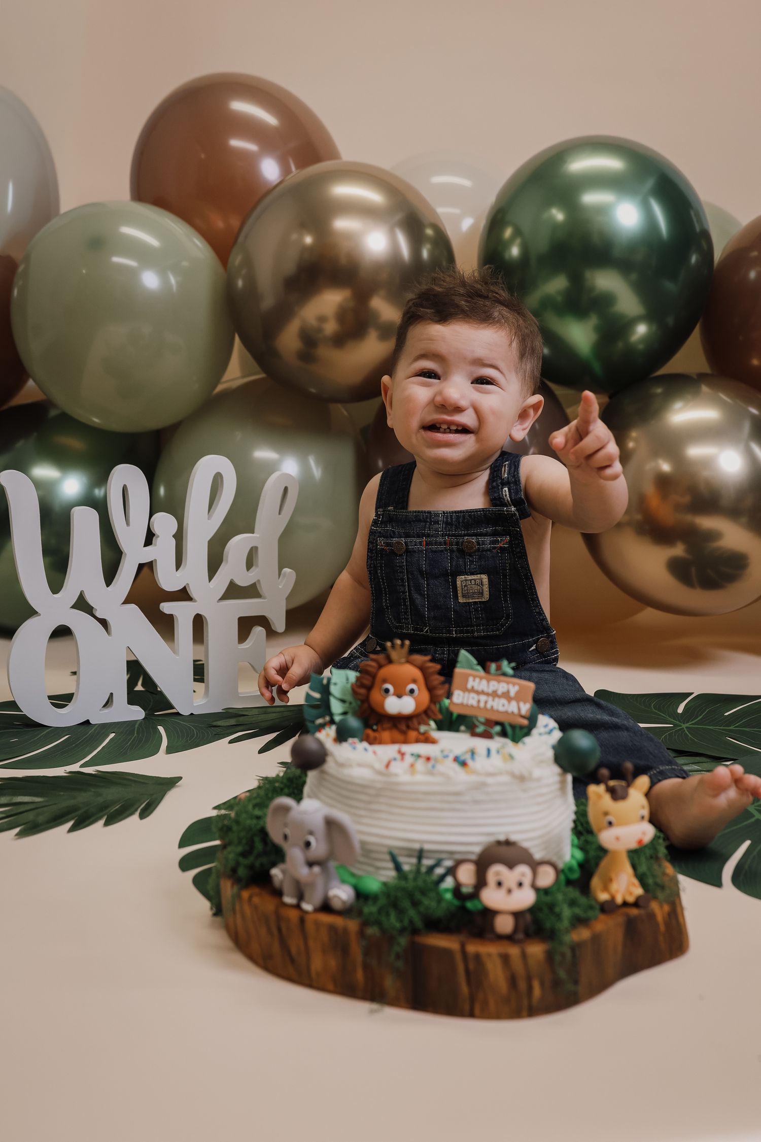 Jungle-themed first birthday party setup with wooden cake stand, safari animal decorations, and metallic balloons.