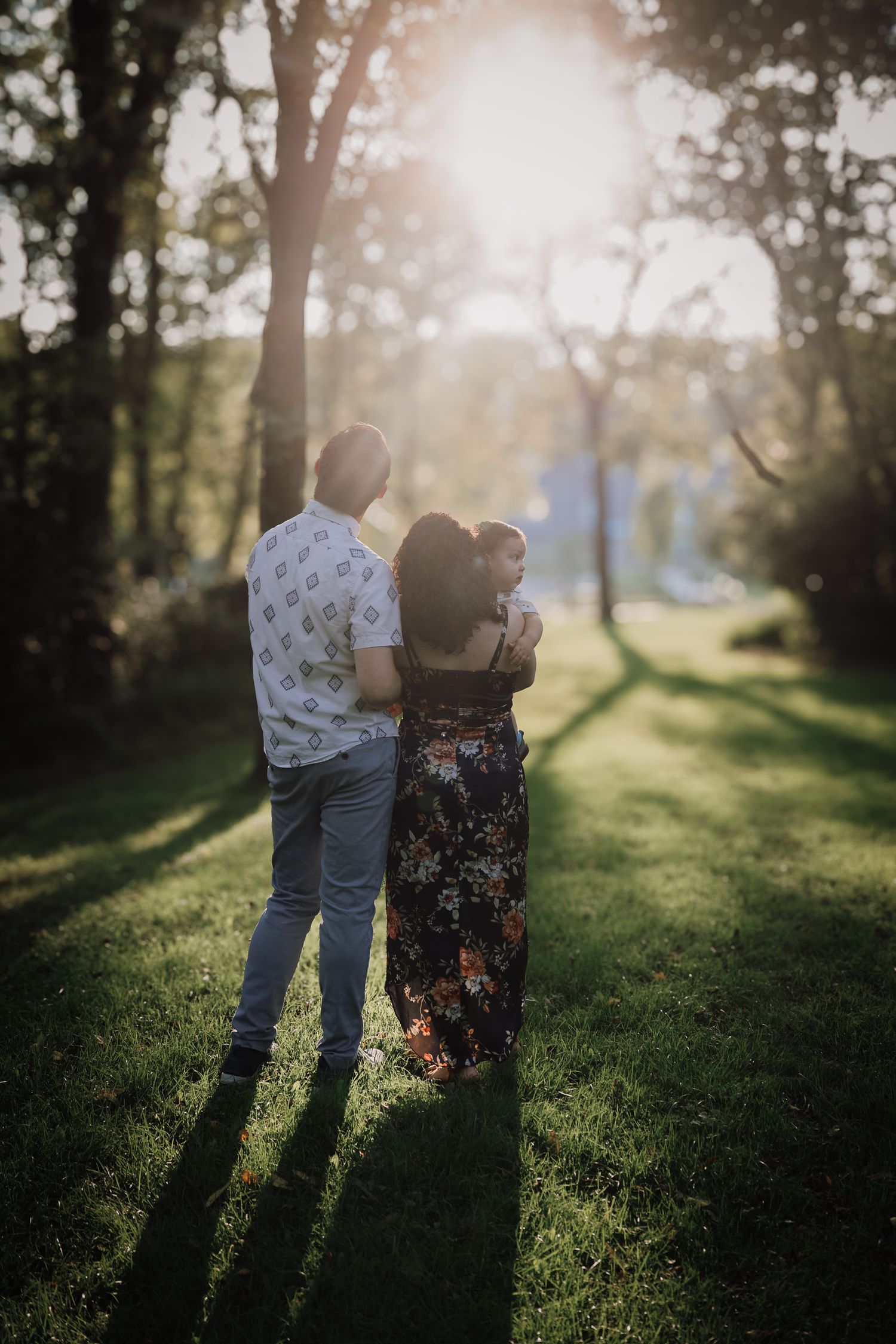 A couple stands together in a sunlit meadow casting long shadows across green grass during golden hour.