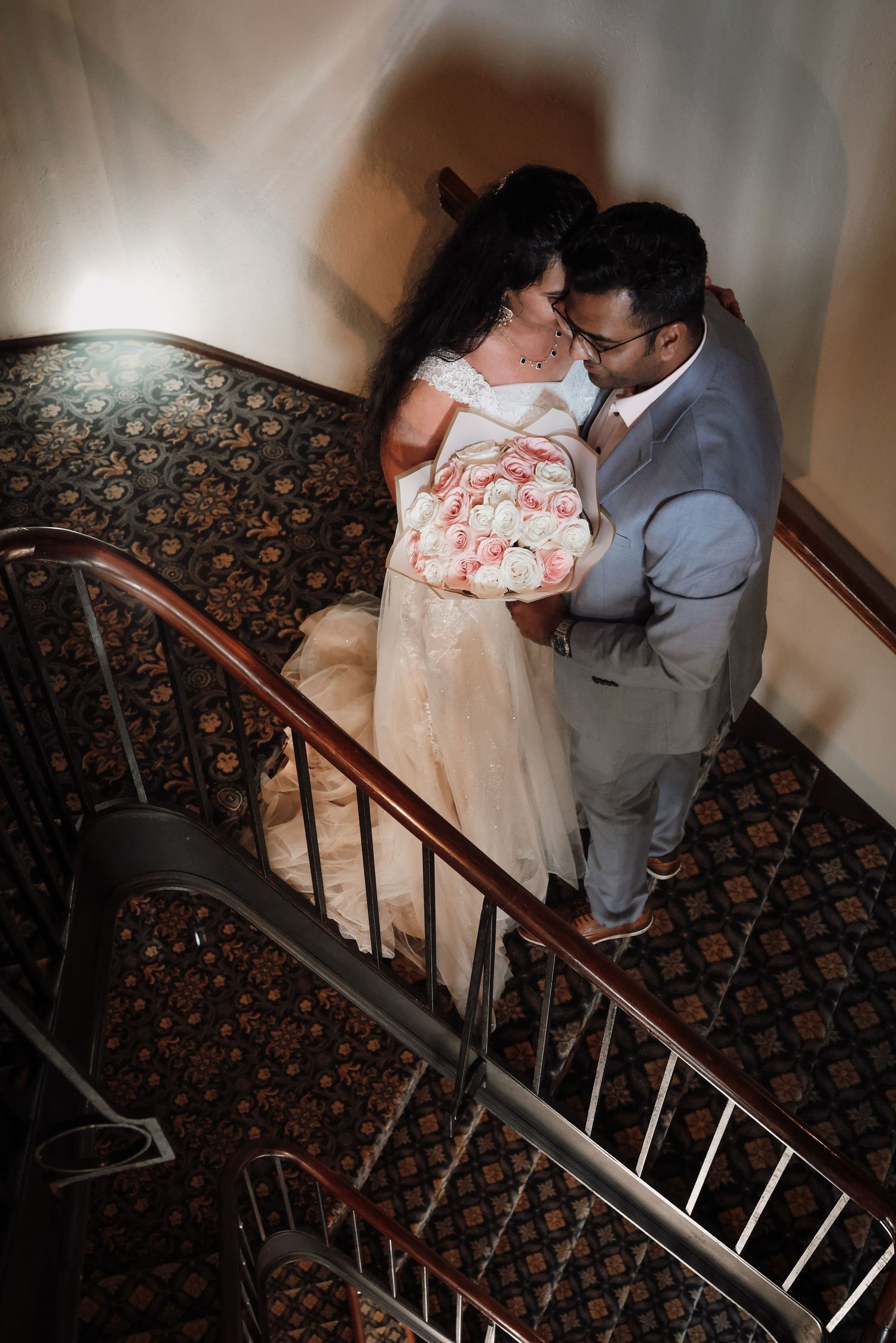A couple in formal attire descends an ornate staircase with patterned carpet in a series of romantic poses.