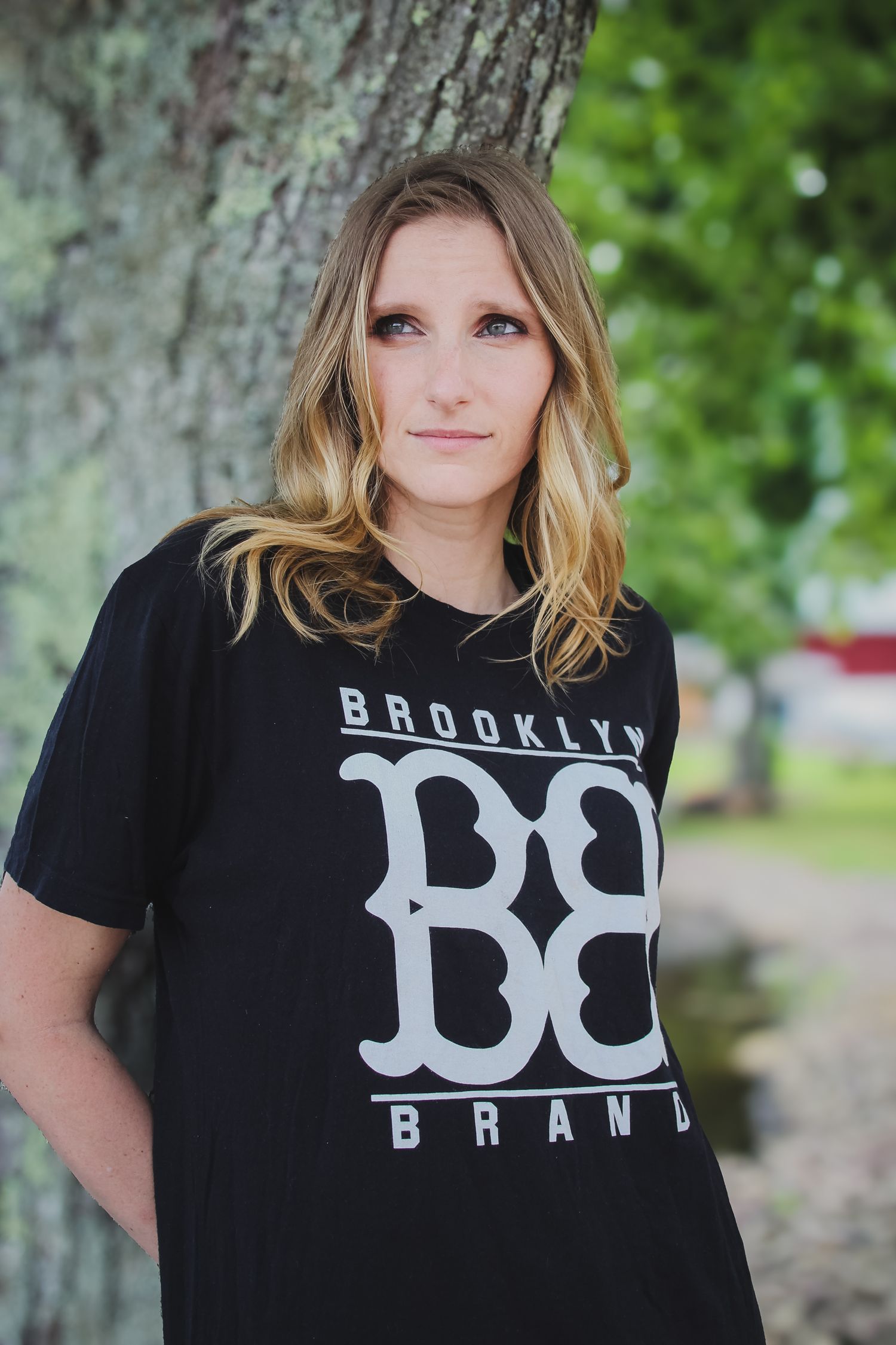 Person wearing a black Brooklyn Brand t-shirt with white lettering poses against a blurred outdoor background.