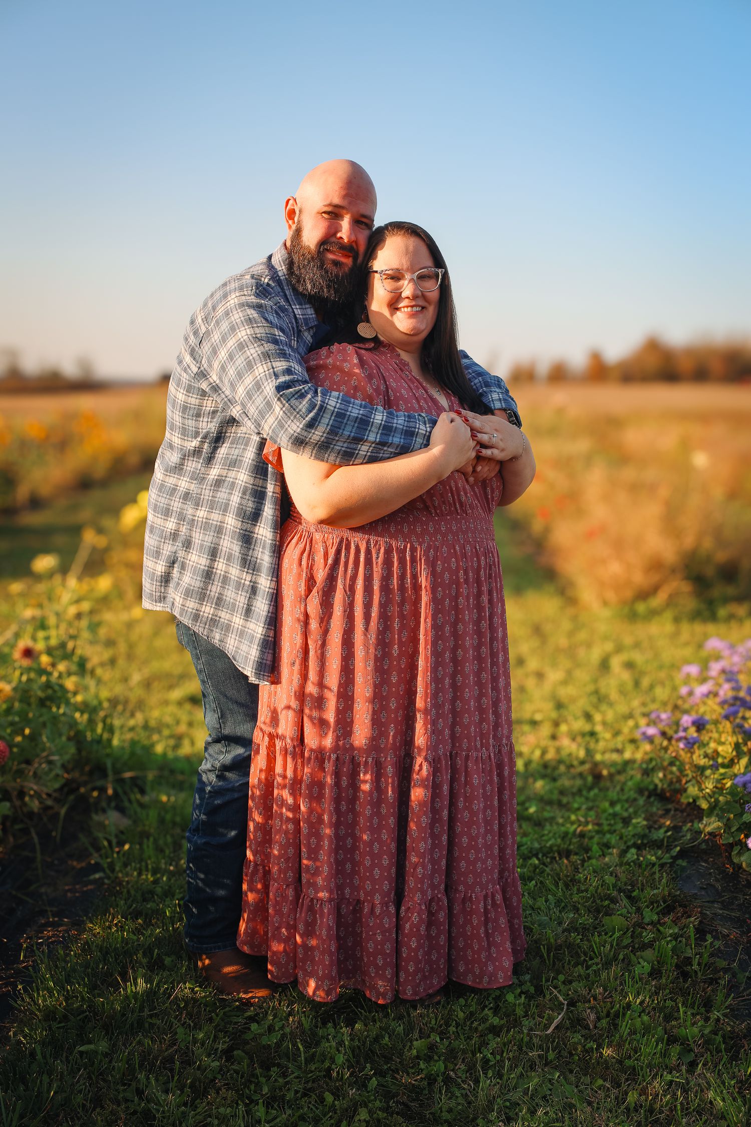 A couple embraces in a wildflower field during golden hour with sunflowers in the background.
