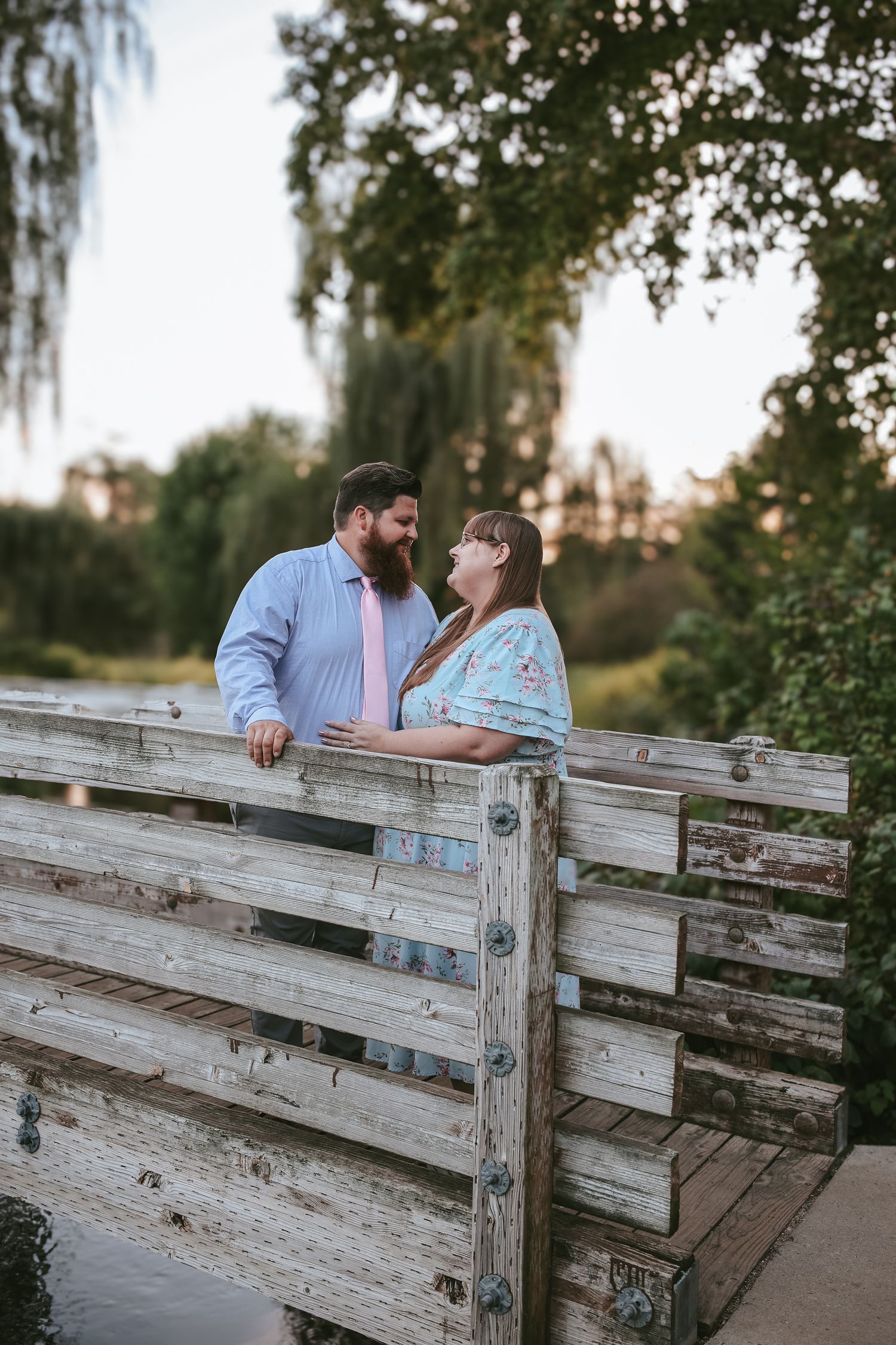 Romantic couple shares intimate moment while leaning on weathered wooden fence during golden hour sunset.