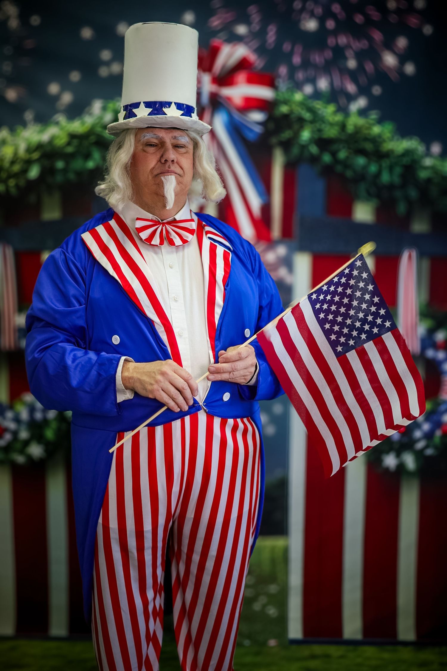 Man dressed as Uncle Sam holding American flag with fireworks and patriotic decorations in background.