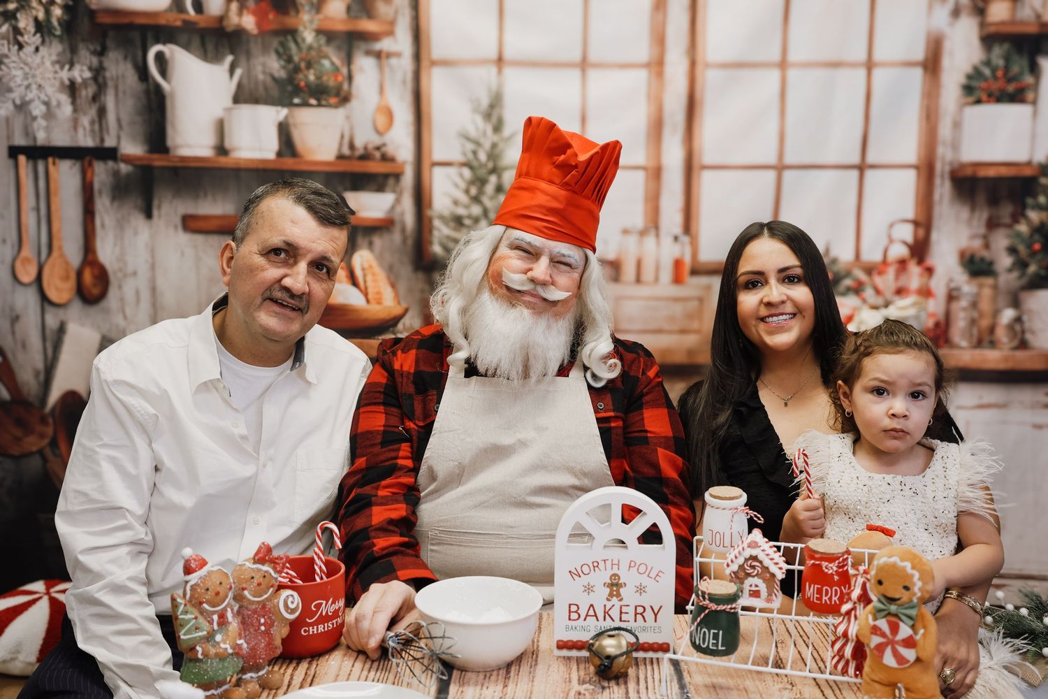 Family posing with Santa Claus in a festive Christmas bakery setting with holiday decorations.