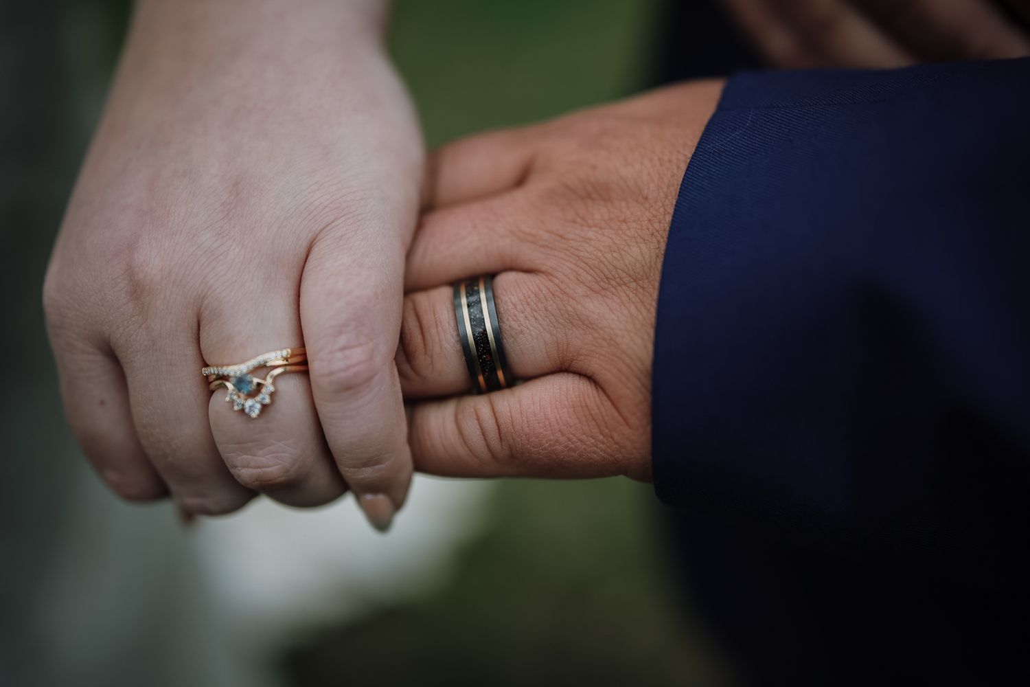 Close-up of couple holding hands showing elegant diamond engagement ring and black wedding band on wedding day.