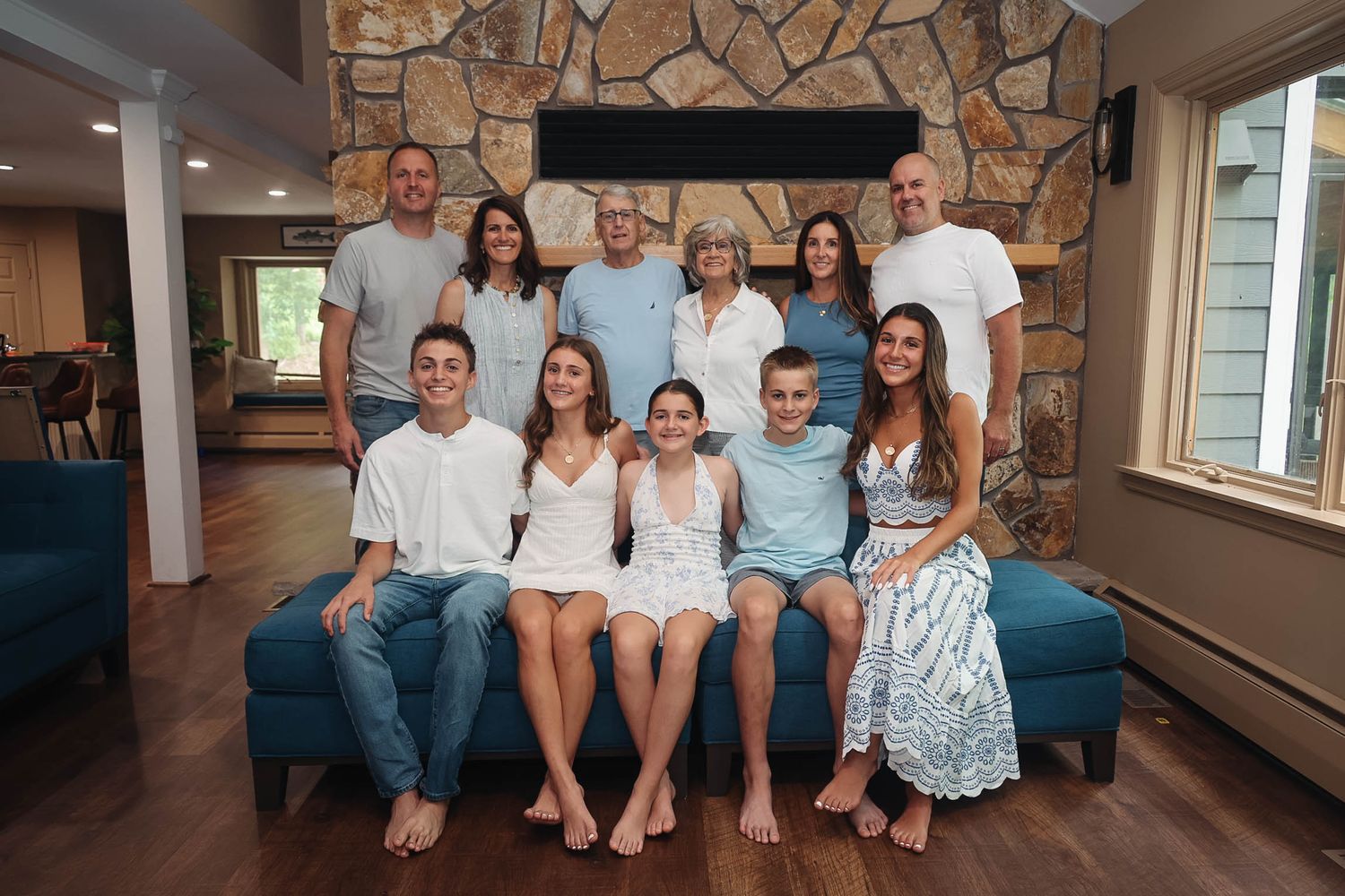 Large family group portrait with adults and teens posing together on a blue sofa in front of a stone fireplace.