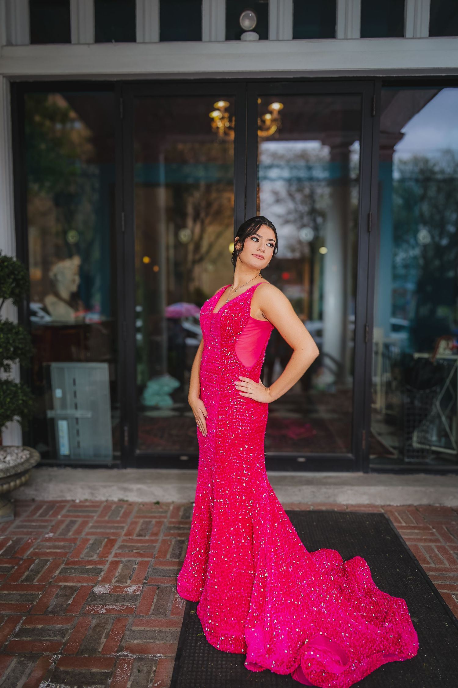 Woman in a stunning hot pink sequined mermaid gown posing elegantly outside a building.