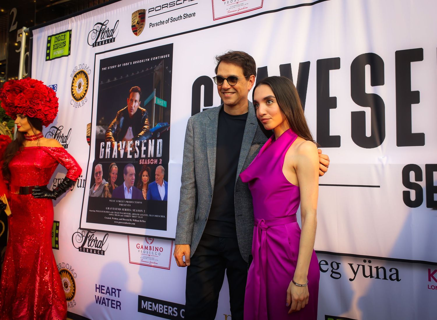 People walking and posing at a movie premiere or red carpet event with promotional posters and signage in the background.