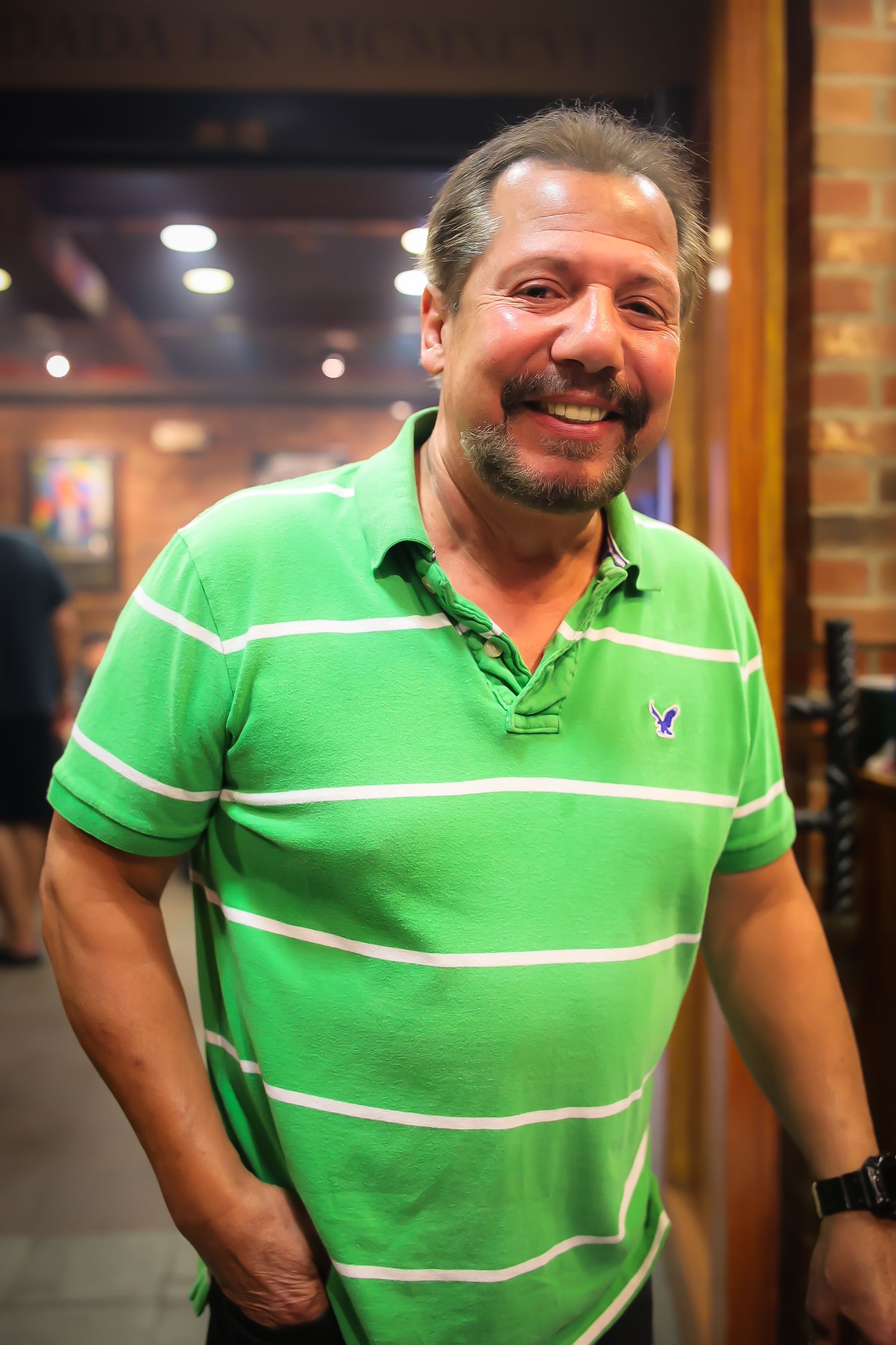 A person wearing a bright green polo shirt with white stripes stands in an indoor setting with warm lighting.