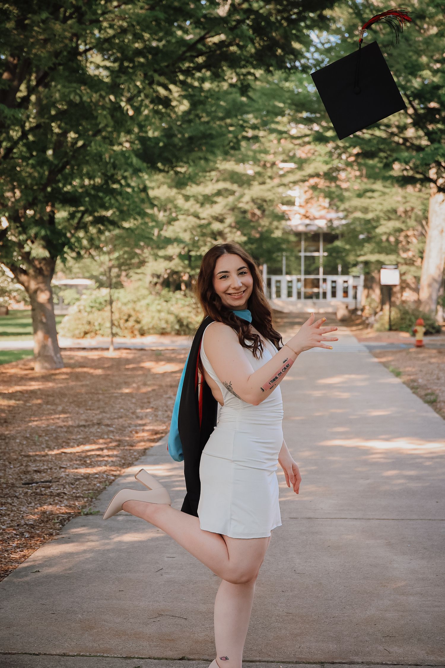A dancer in a white dress performs graceful movements on a tree-lined path during a summer photoshoot.