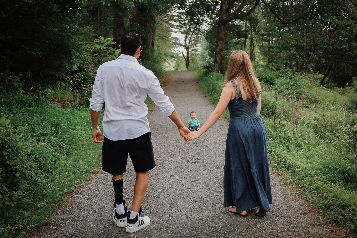 People walking hand in hand along a tree-lined path on a summer day.