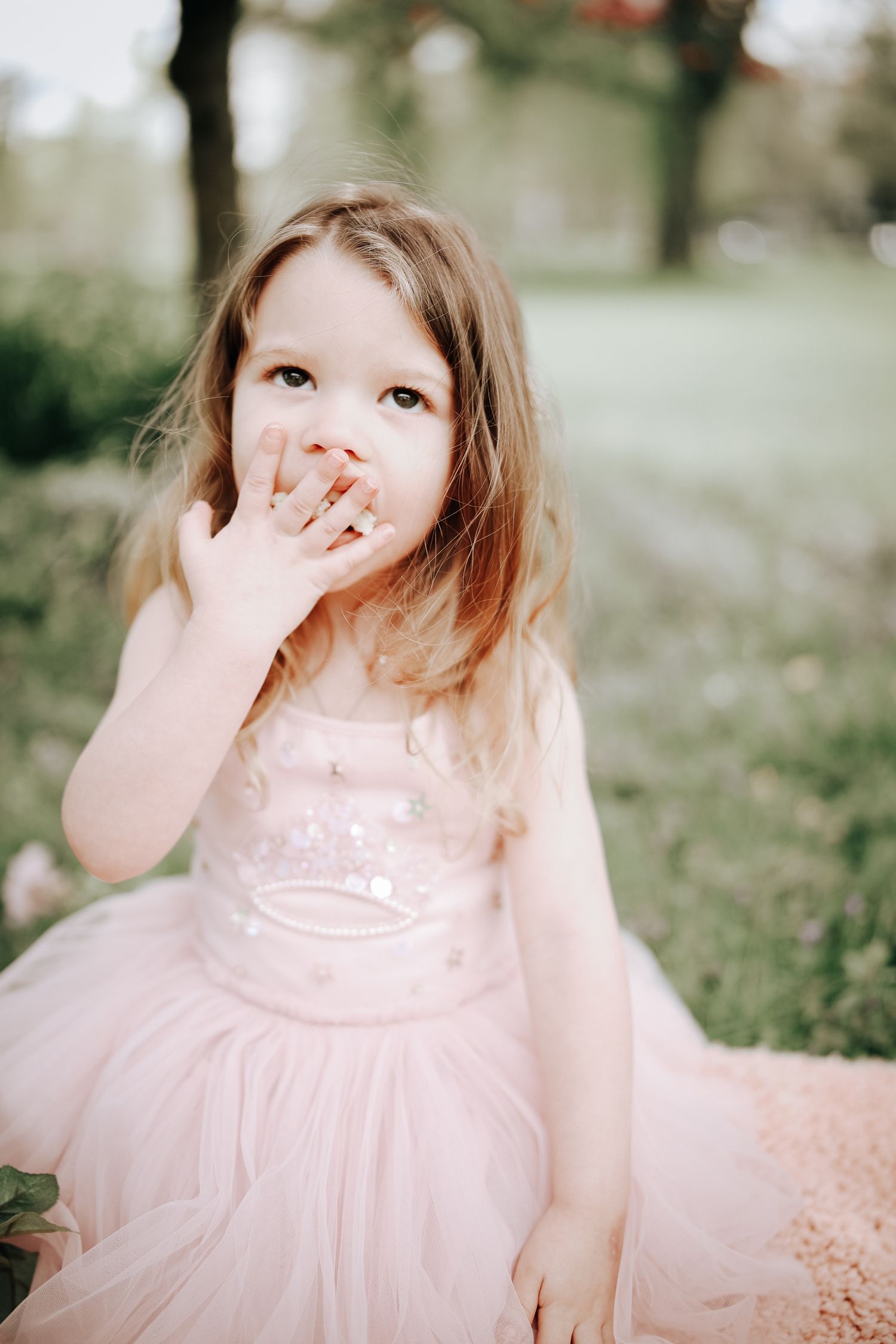 A series of four photos showing a child in a pink tulle dress covering their mouth while giggling playfully outdoors.