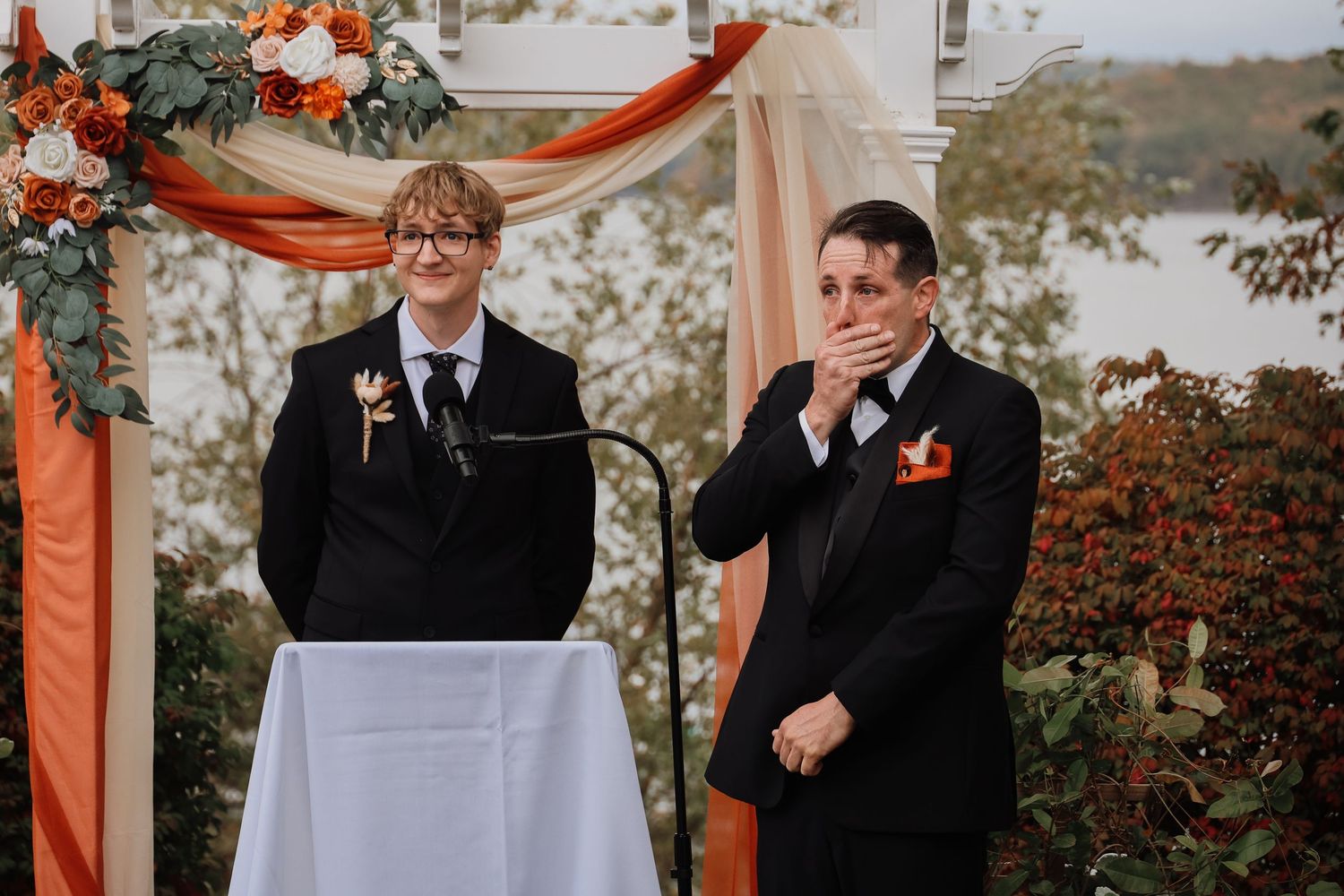 Outdoor autumn wedding ceremony with orange and peach draping decor and floral arrangements.