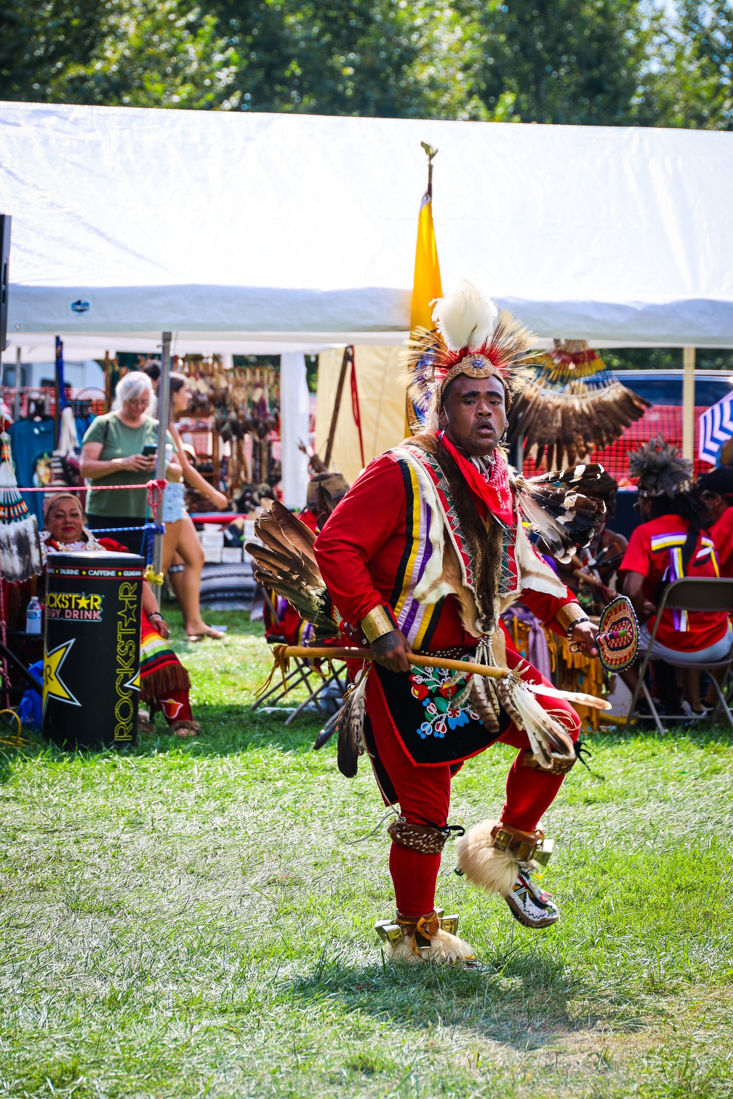 Native American dancers in traditional red regalia perform energetic ceremonial dances at an outdoor cultural festival.