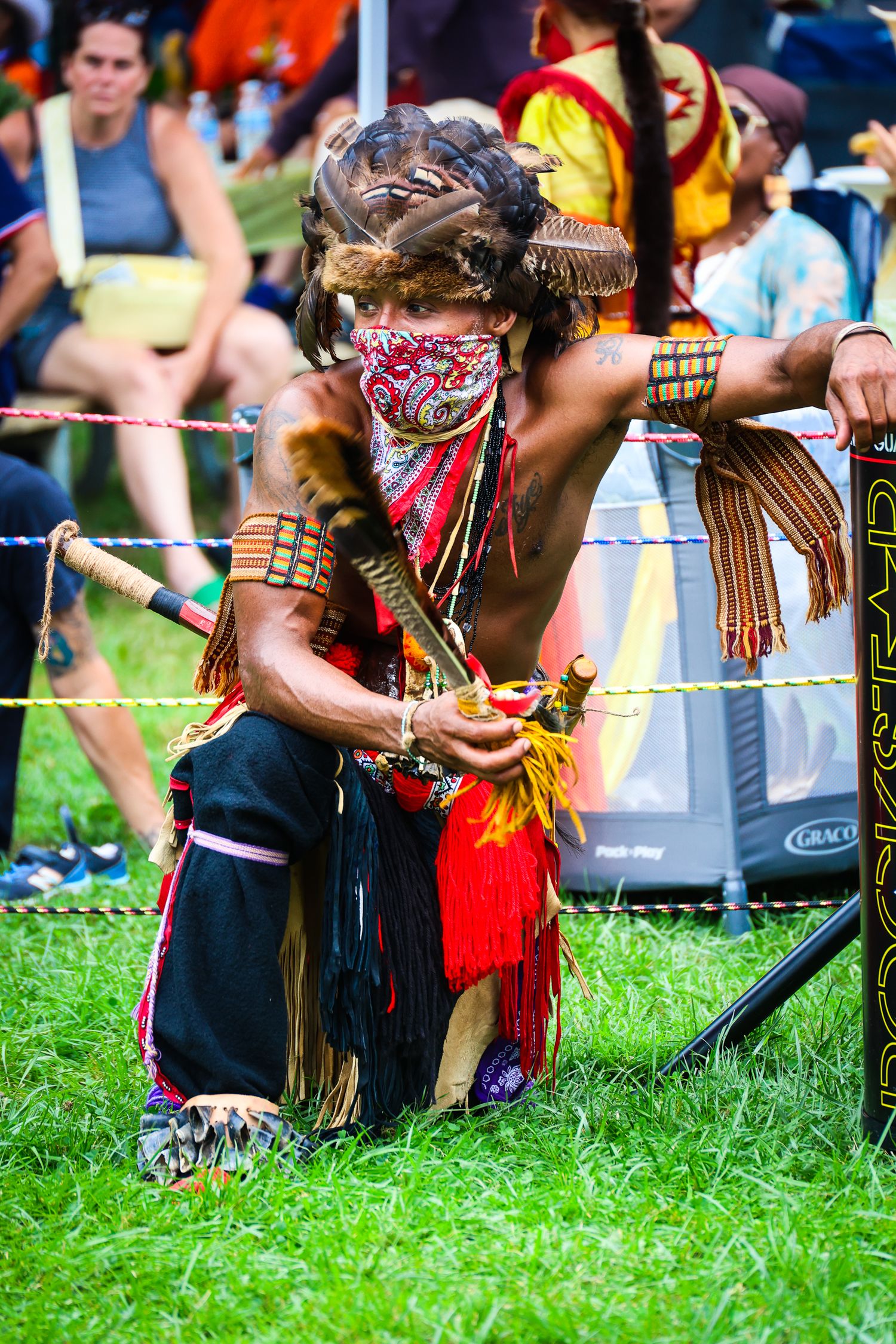 Native American dancers in traditional regalia perform on grass at an outdoor cultural festival.