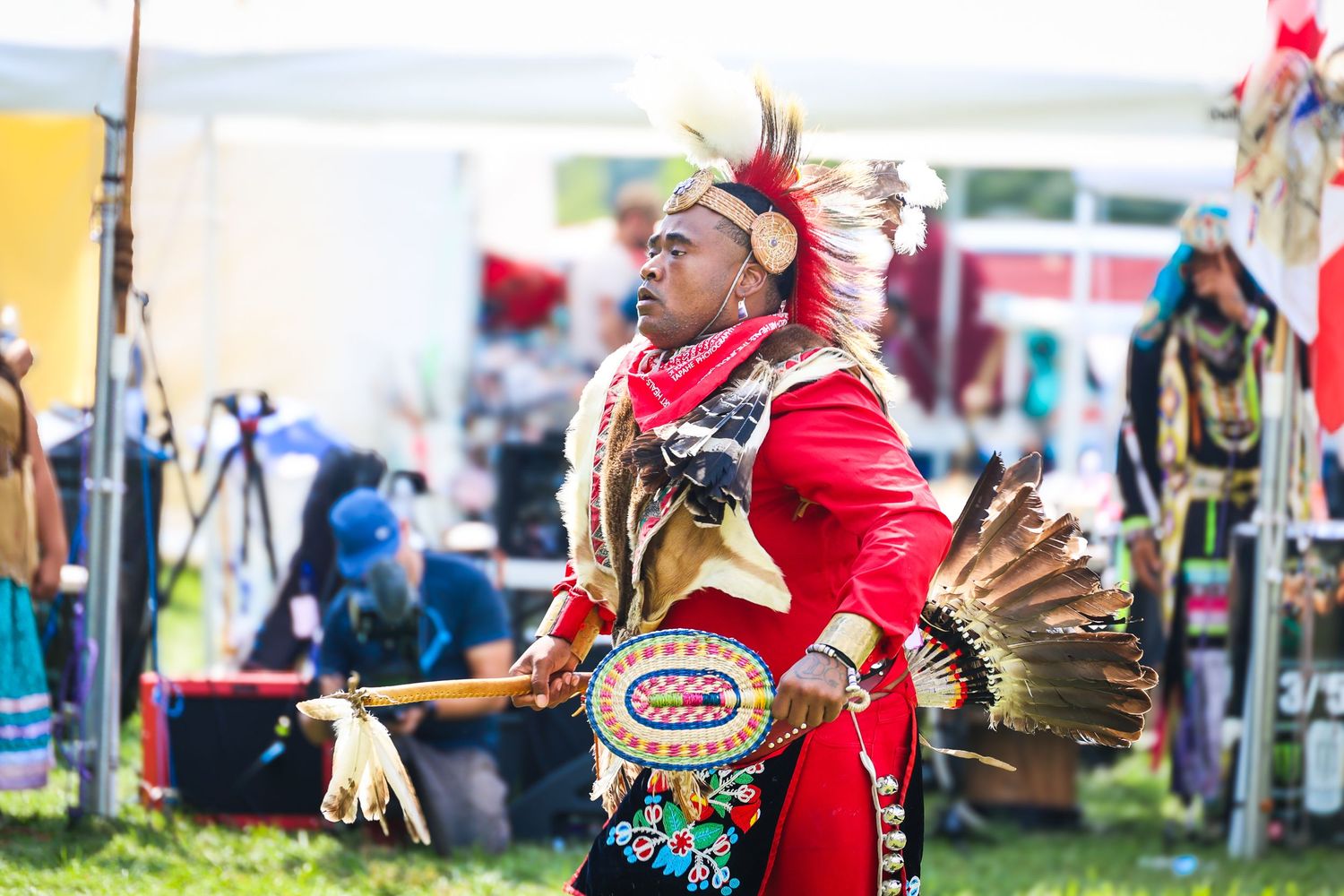 A performer in a red cape and traditional regalia dances during a cultural celebration event.