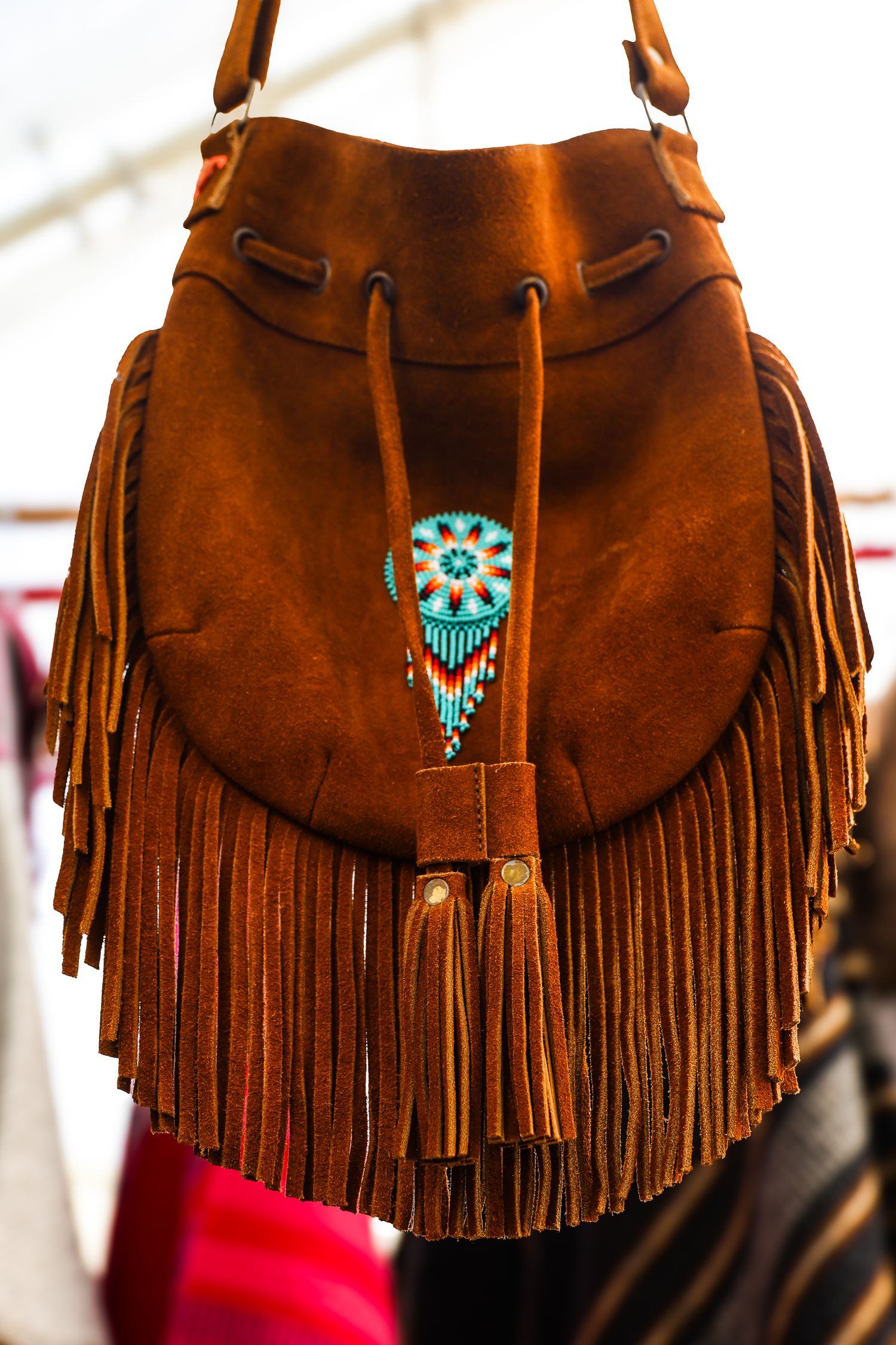 Close-up of brown leather fringe bags with turquoise Native American style beaded decorations displayed in a row.
