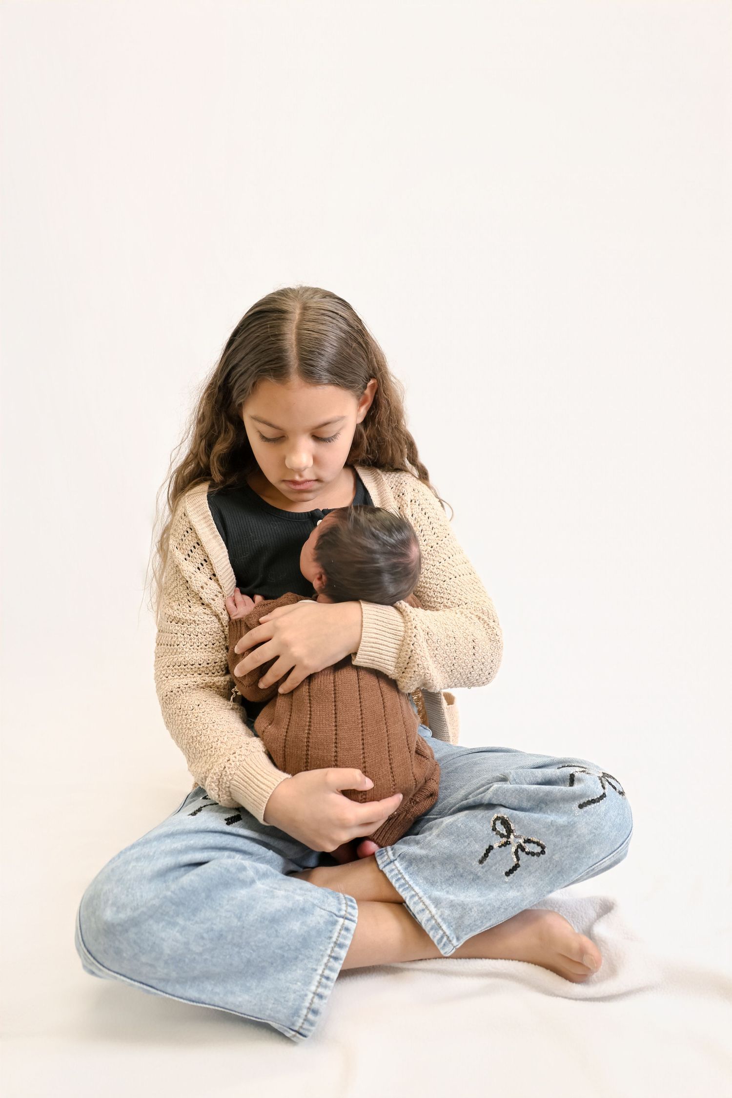 Three photos of someone in a cream sweater and jeans sitting cross-legged while cuddling a black cat against a white backdrop.