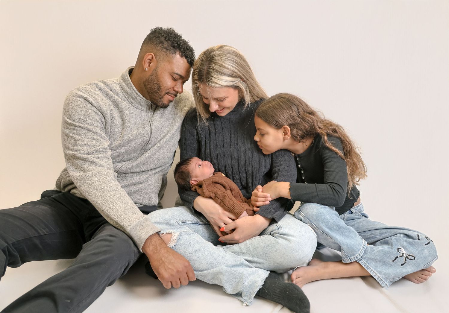A group of people cuddle together while lying down on a light colored floor in matching grey and black outfits.