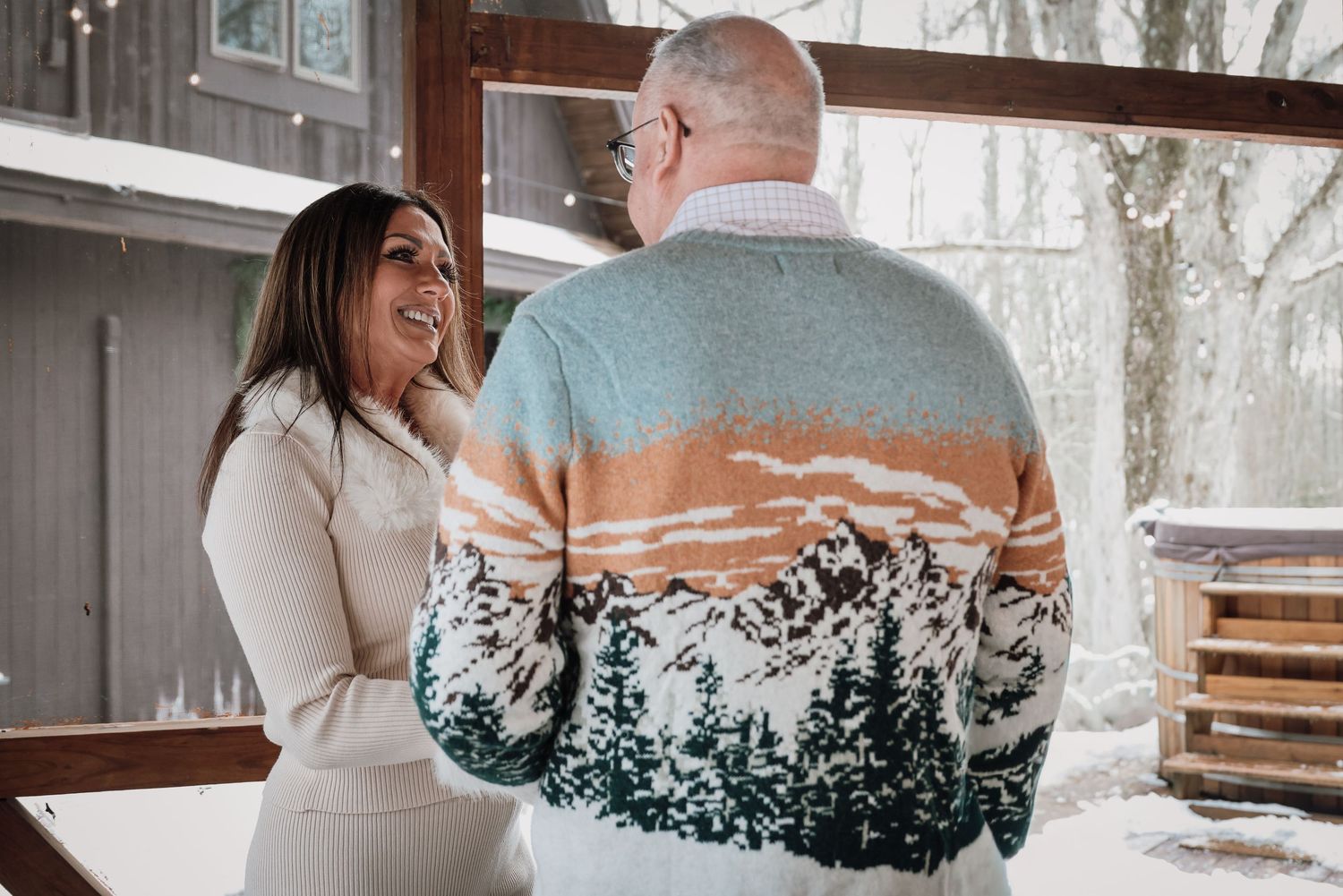 A couple embraces while wearing a unique sweater featuring a forest landscape design on the back.