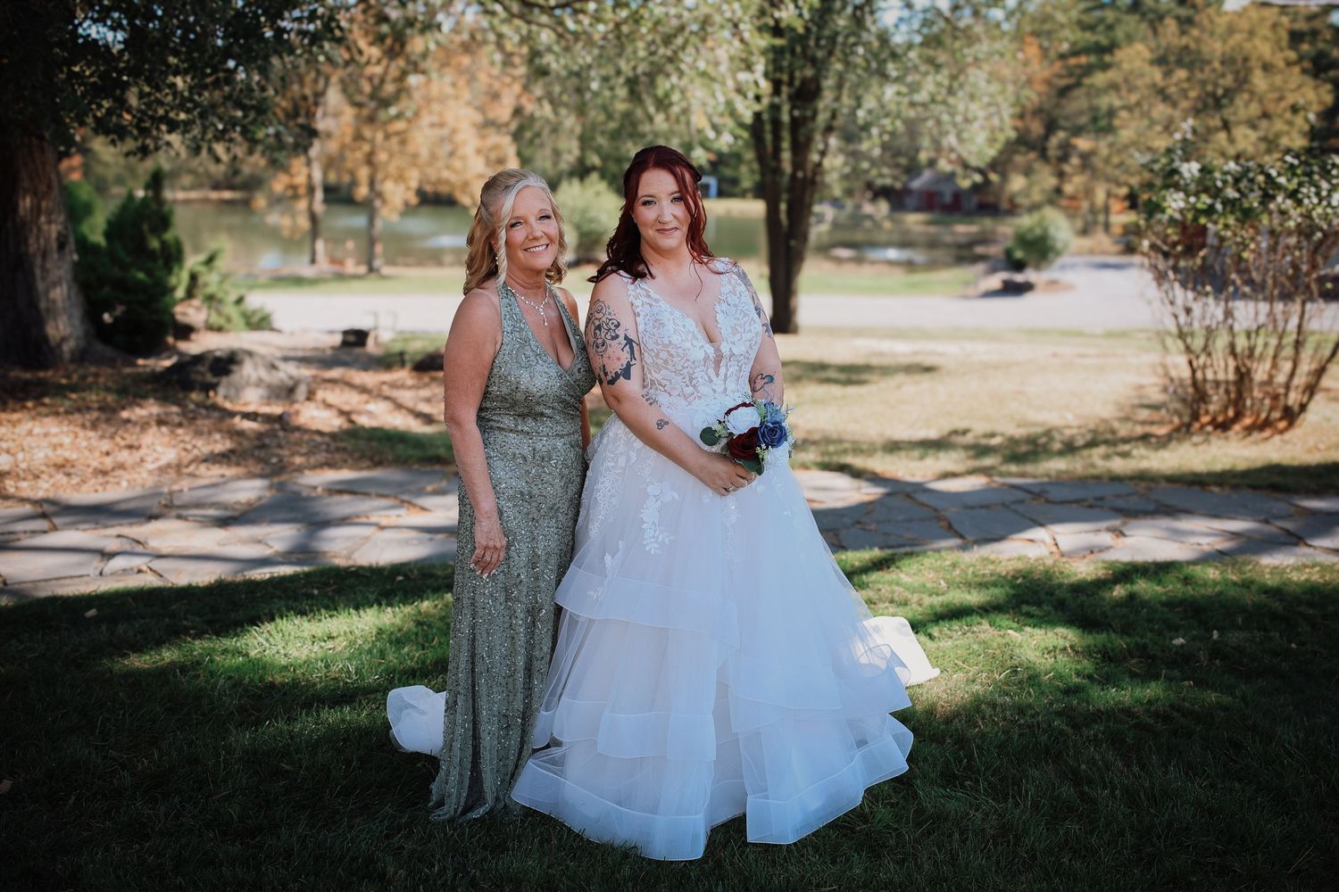 A group of people in formal attire gather outdoors for a wedding photo session in a sunny garden setting.