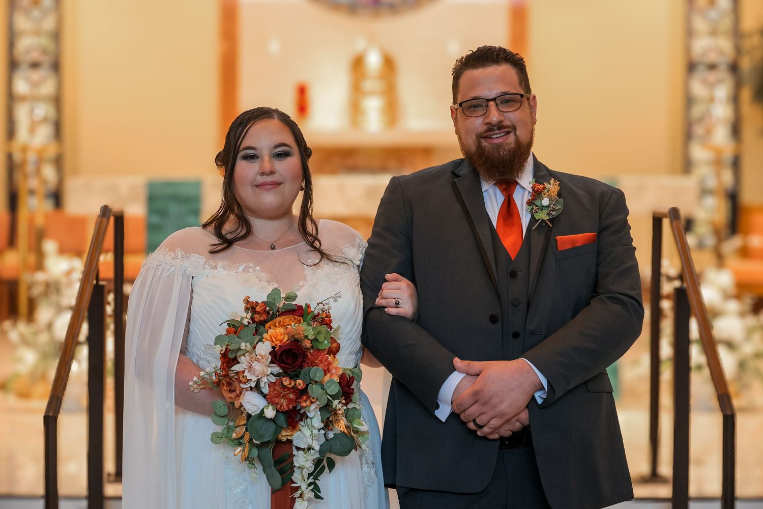A couple stands at the altar during their wedding ceremony, with the bride holding a vibrant orange and blue bouquet.