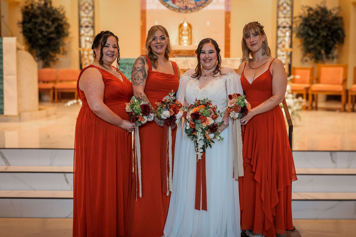 A wedding party in a church with bridesmaids wearing matching red dresses and holding colorful bouquets.