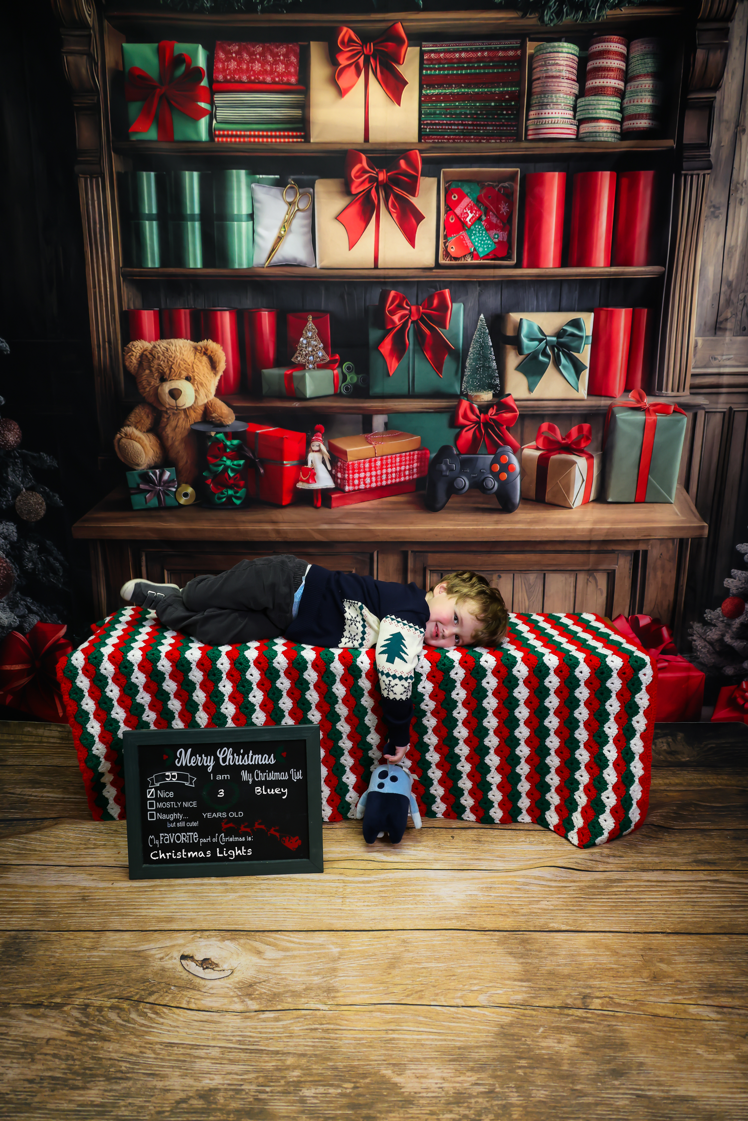 Christmas studio setup with red wrapped presents, teddy bears, and a black chalkboard sign on wooden floor.