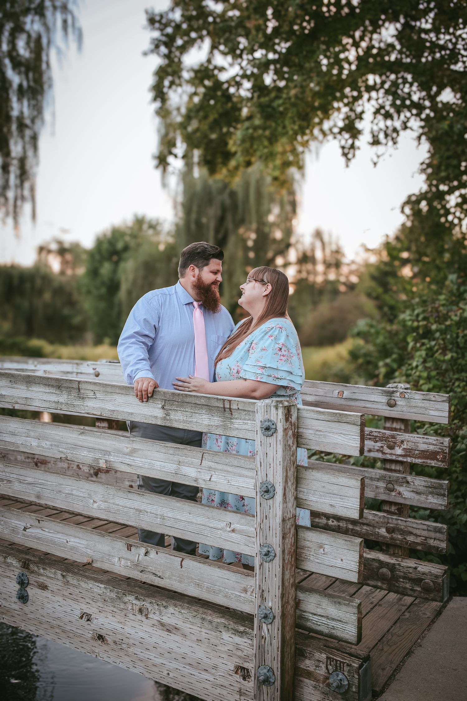Couple sharing a romantic moment together by a rustic wooden fence in a park setting.