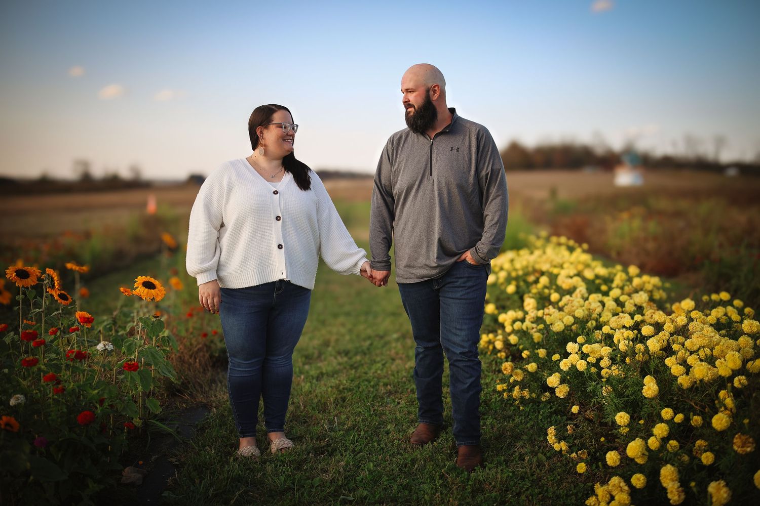 A couple stands together in a field of vibrant wildflowers during golden hour.