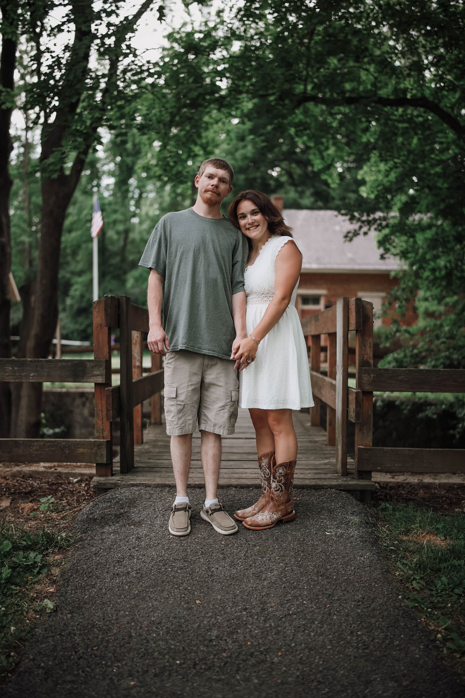 Couple holding hands on a wooden bridge, man in green shirt and woman in white dress with cowboy boots.