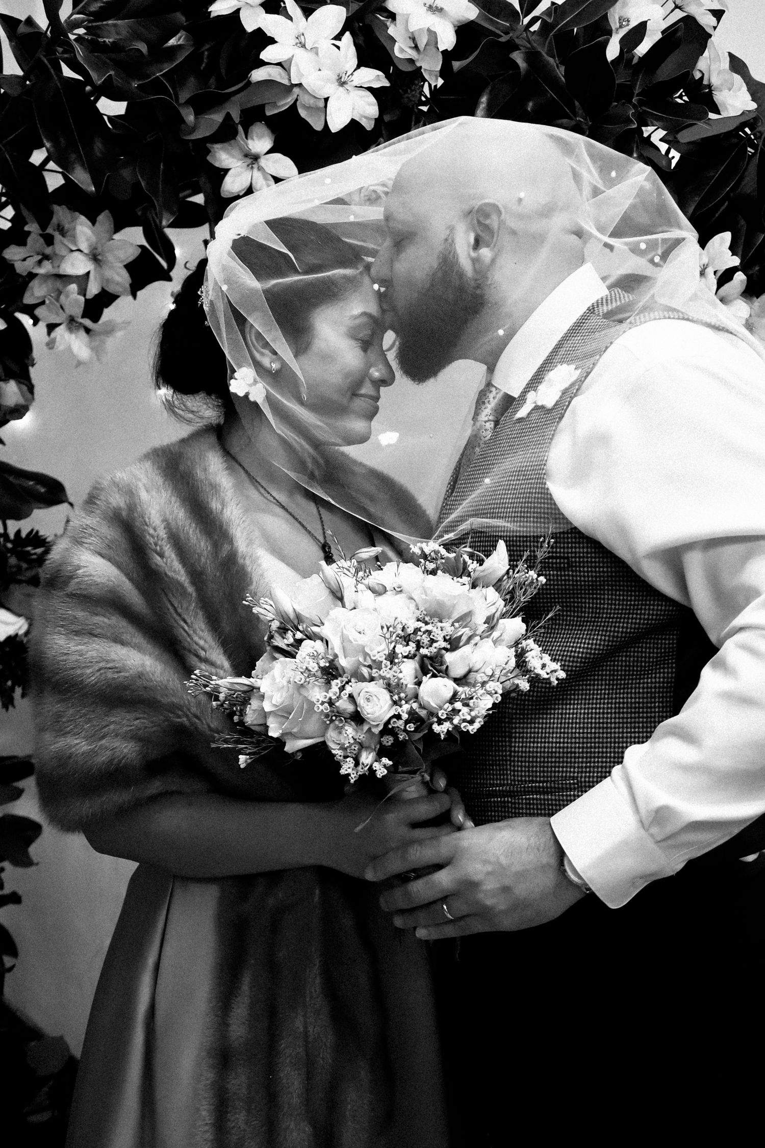 A black and white photo sequence shows a tender embrace between a couple holding a bouquet at their wedding ceremony.