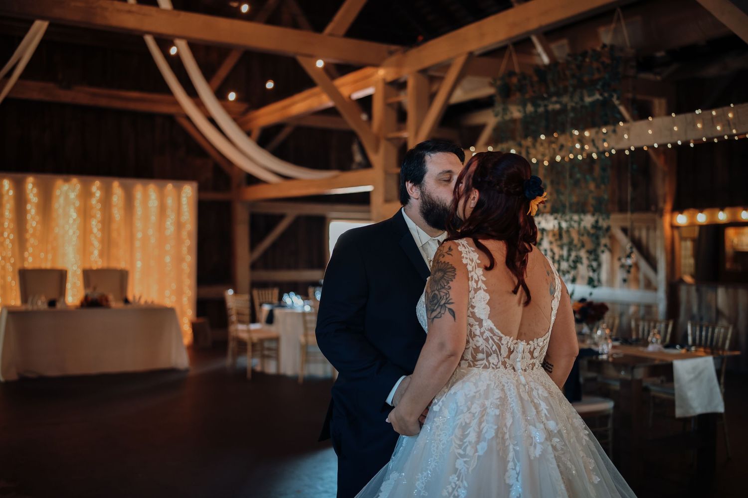 Newlyweds share a romantic moment during their first dance under twinkling lights at an elegant barn reception.
