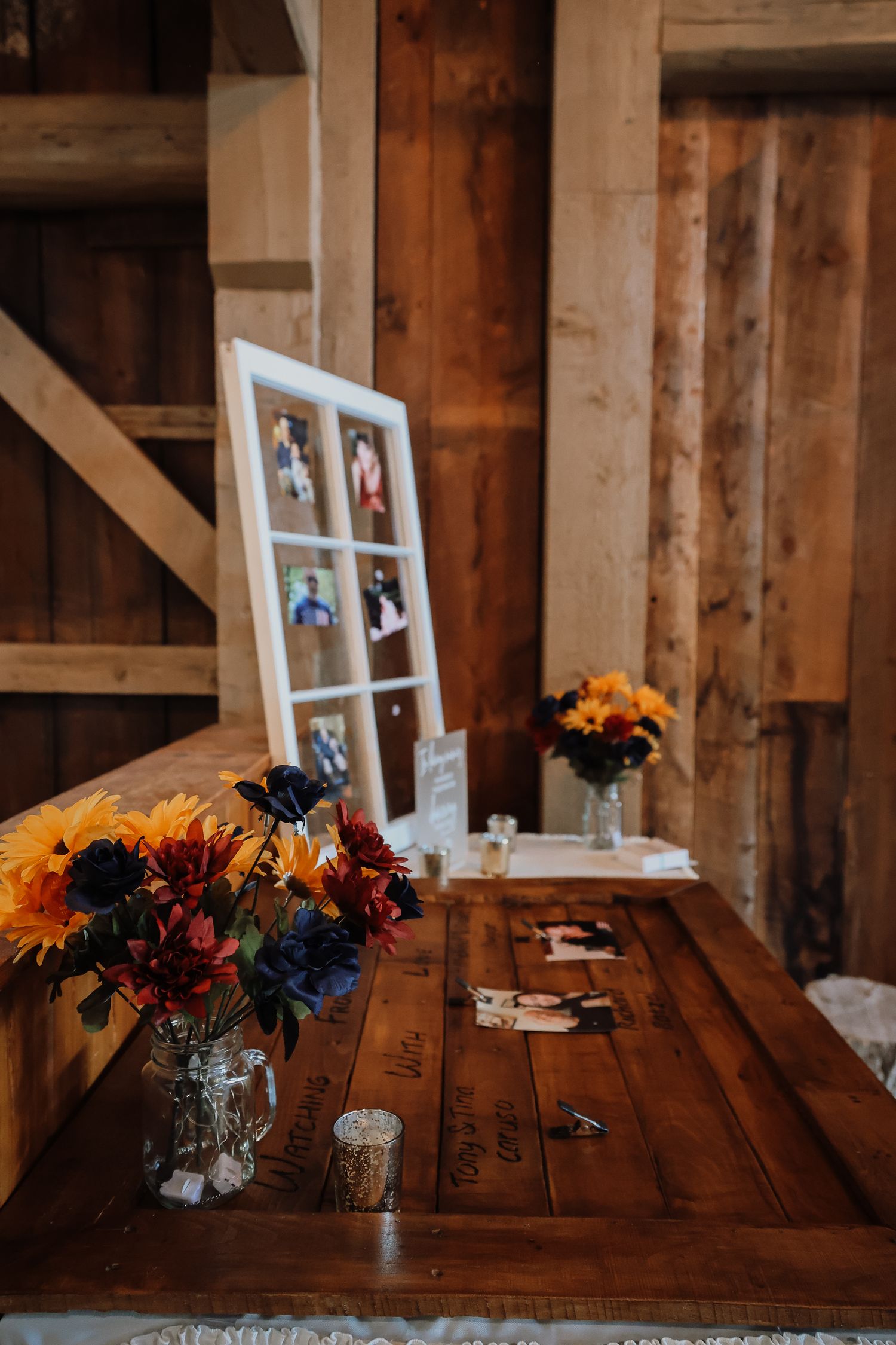 Rustic wooden table with floral centerpieces and framed photos displayed in vintage window panes at a wedding reception.