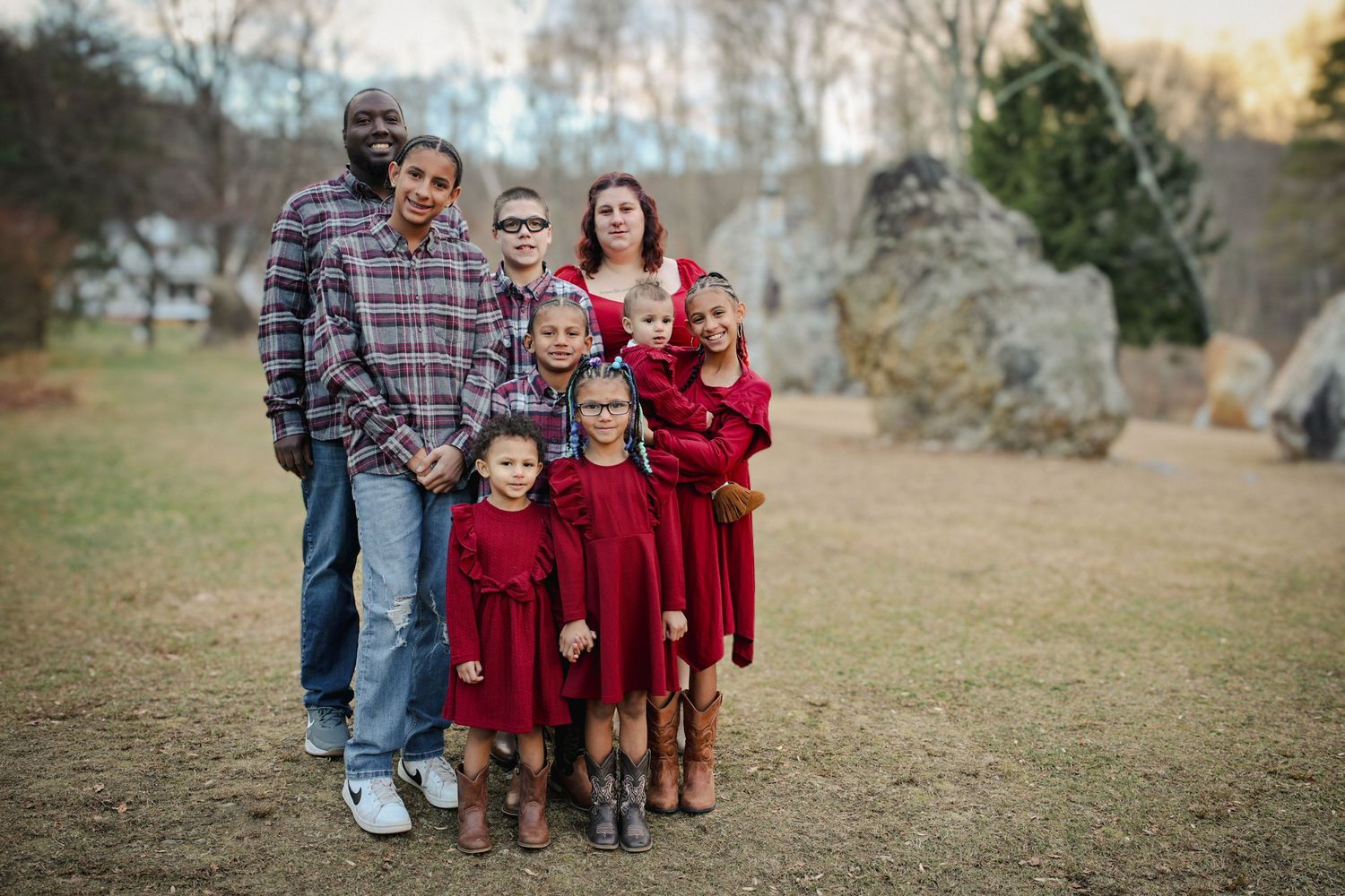 A group wearing coordinated red and plaid outfits poses together in an outdoor autumn setting.