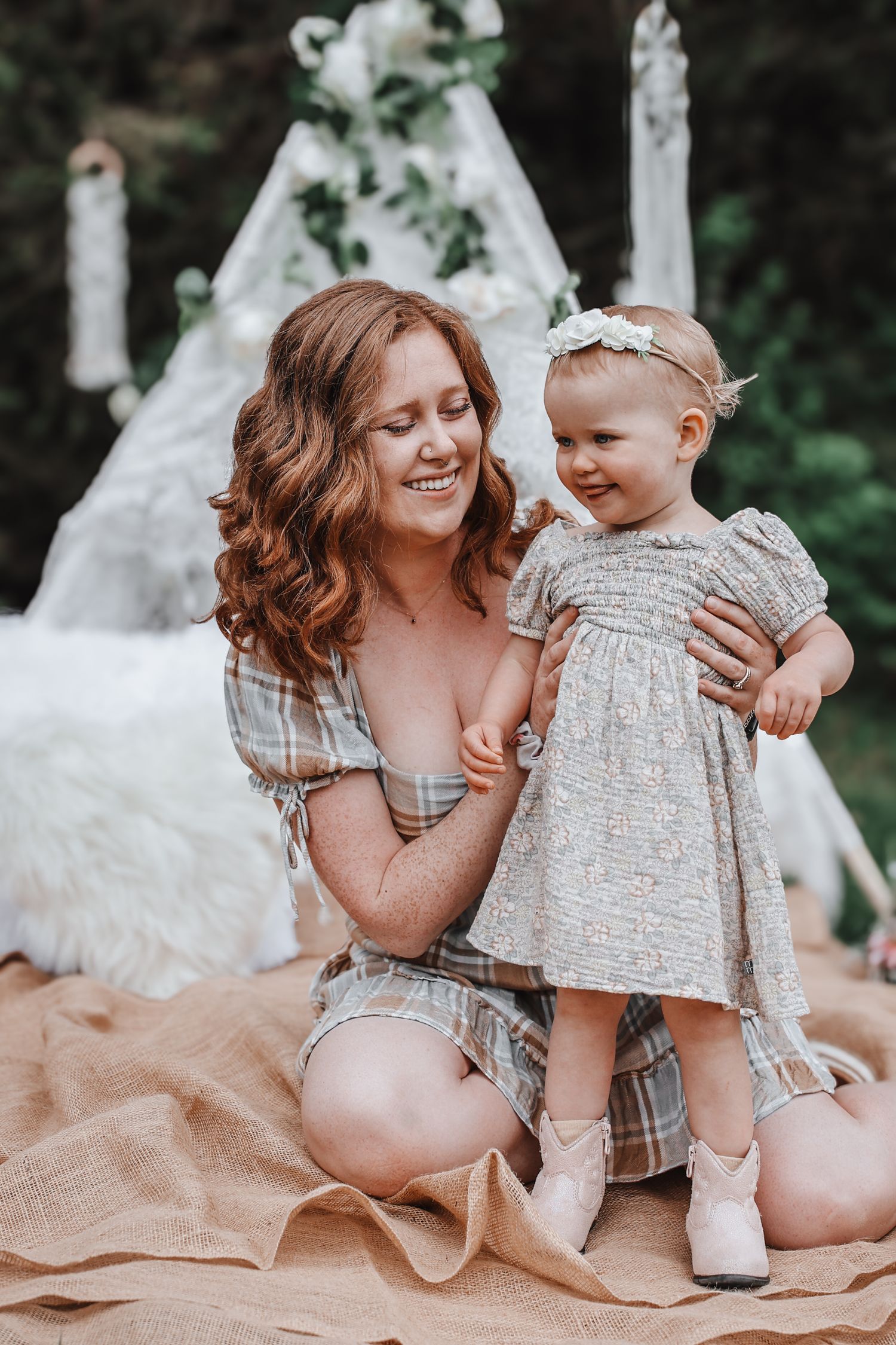 Mother and baby in matching neutral outfits share sweet moments together on a blanket during outdoor photoshoot.