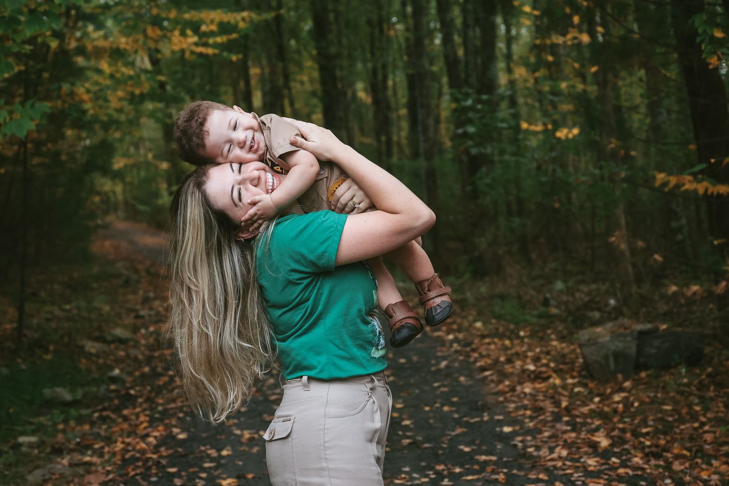 Couple embracing in autumn forest with fallen leaves on ground and green trees in background.
