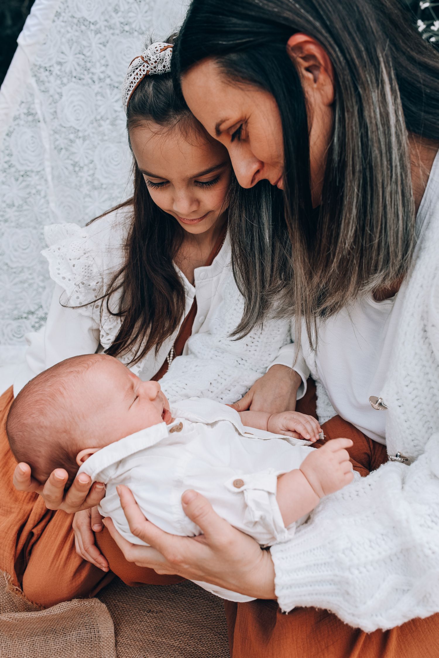 A tender family moment as two people lovingly gaze at a newborn baby wearing white clothing.