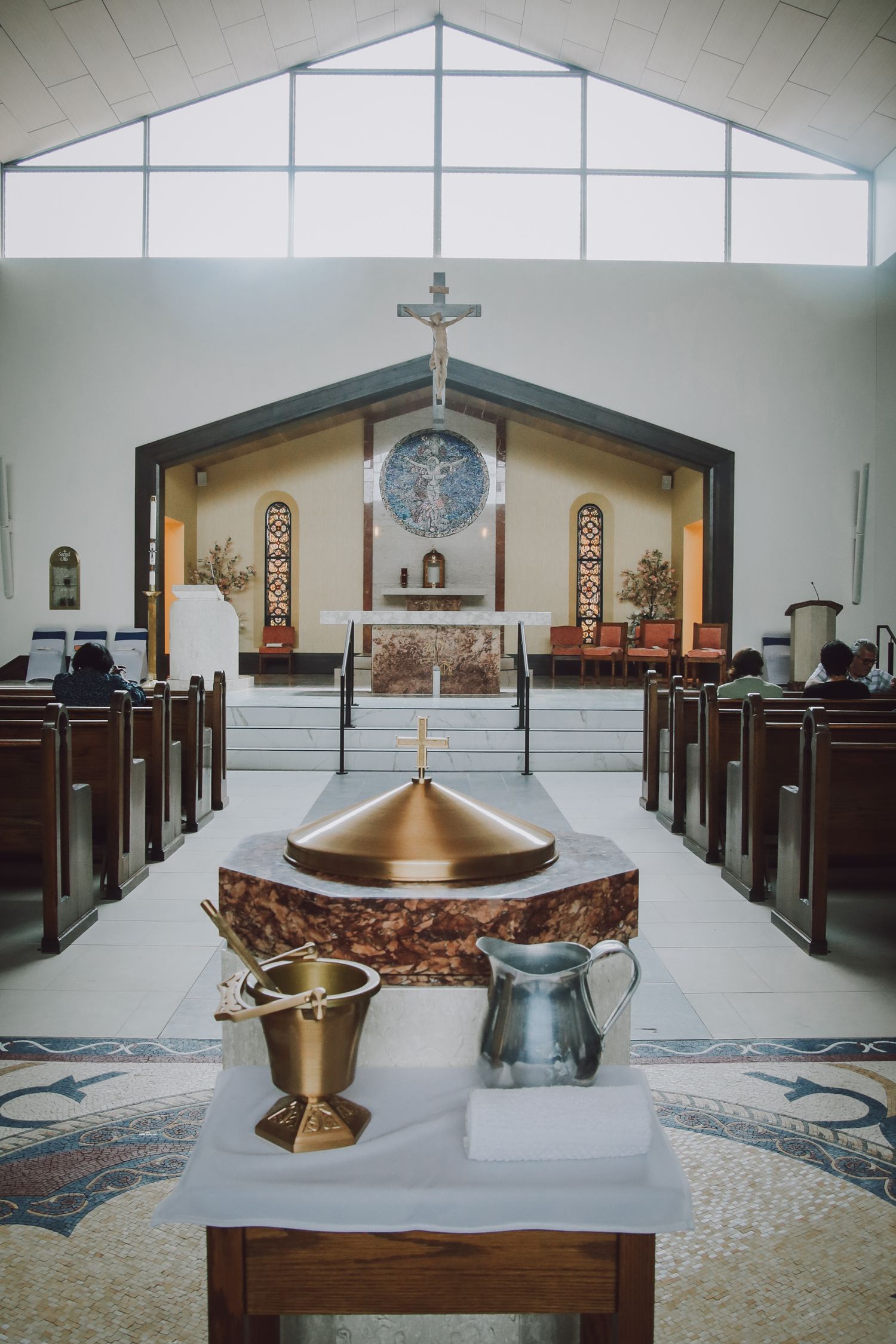 Interior views of a modern church sanctuary showing wooden pews, altar area, and religious symbols in white and gold tones.
