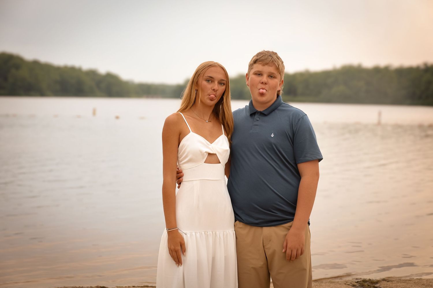 A couple stands together on a beach at sunset in casual summer attire.