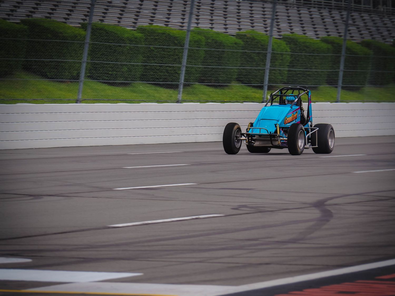 A blue Formula race car speeds along a wet racetrack during a racing competition.