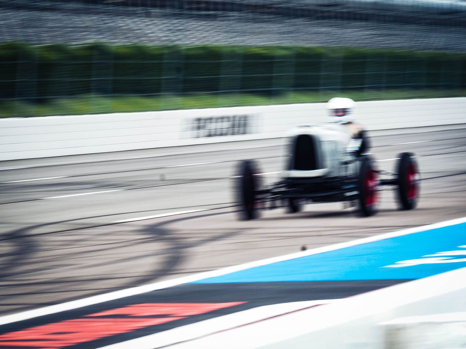 Race cars speed around a curving Formula 1 track with blue and red striped runoff areas during a racing event.