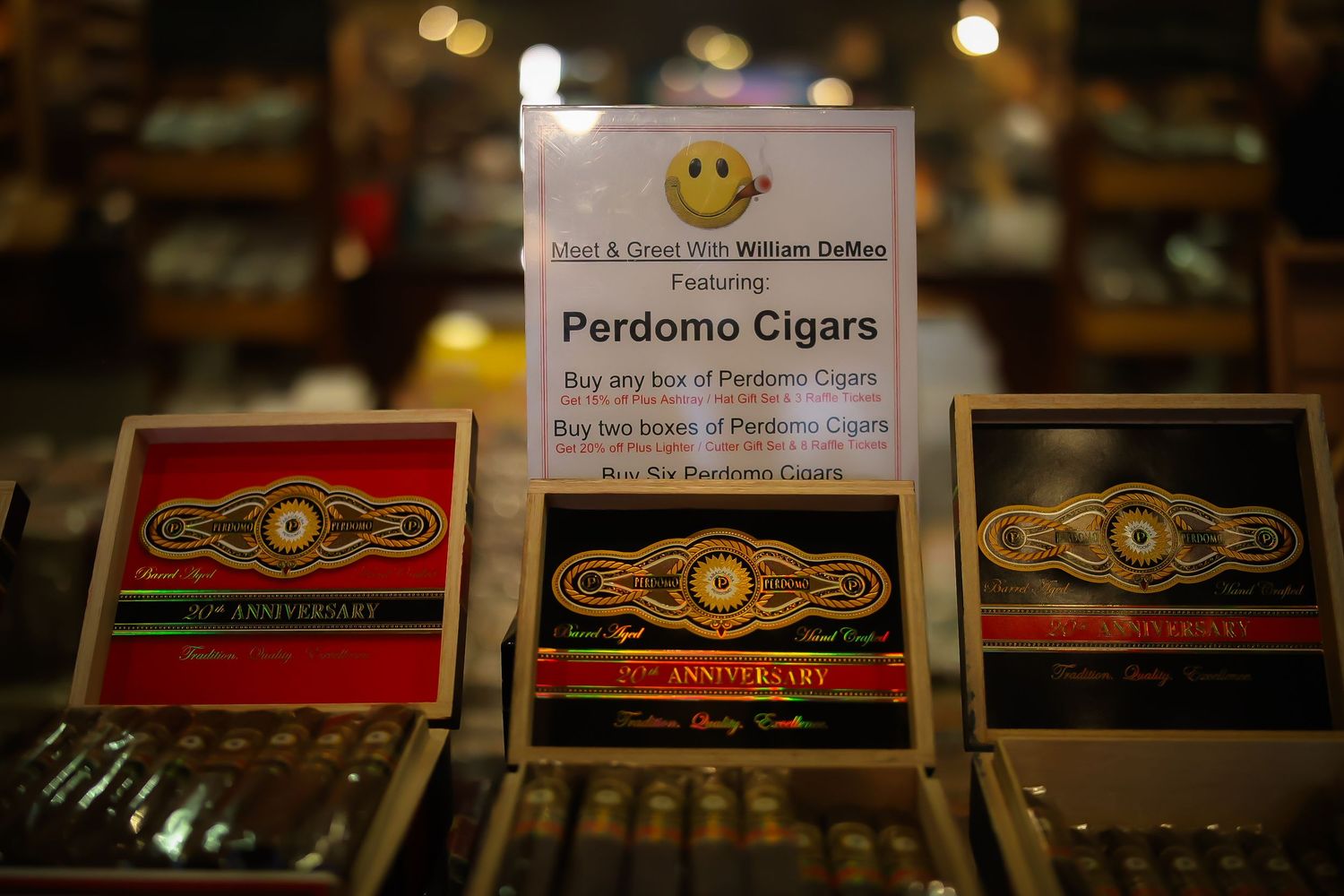 Assorted premium cigar boxes and humidors displayed in a dimly lit retail setting with warm lighting and wooden shelves.