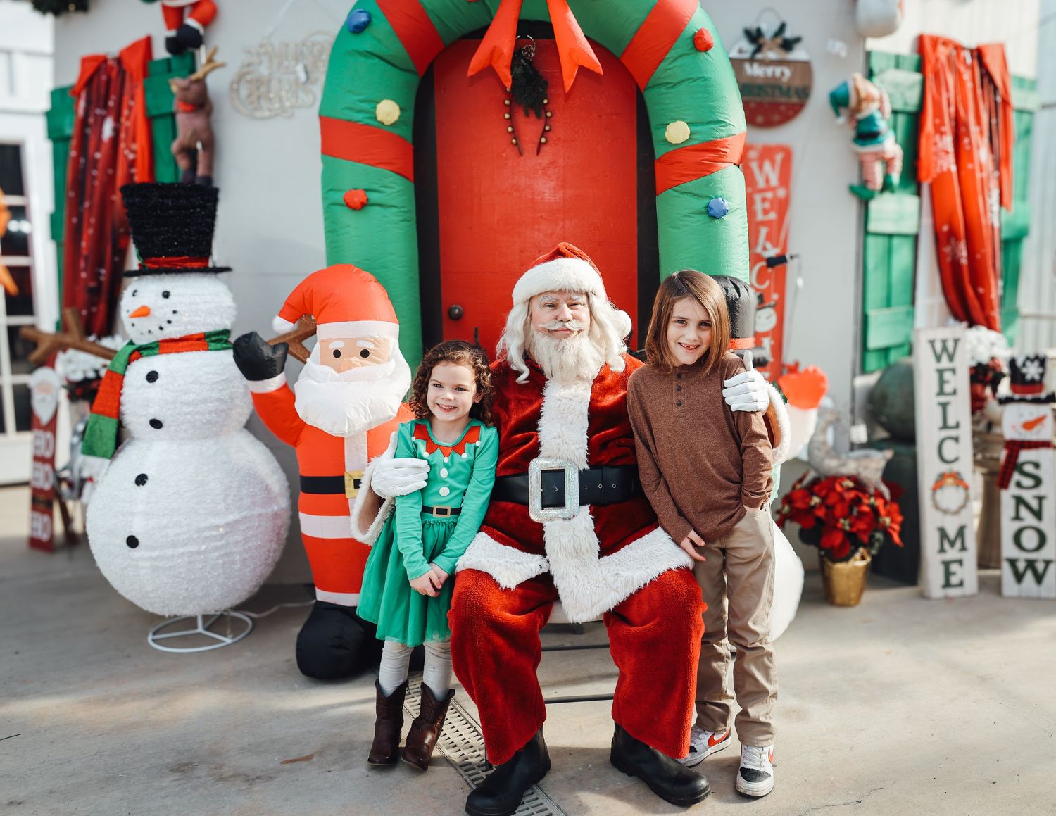 Festive holiday display with inflatable snowman and Santa decorations against a storefront backdrop.