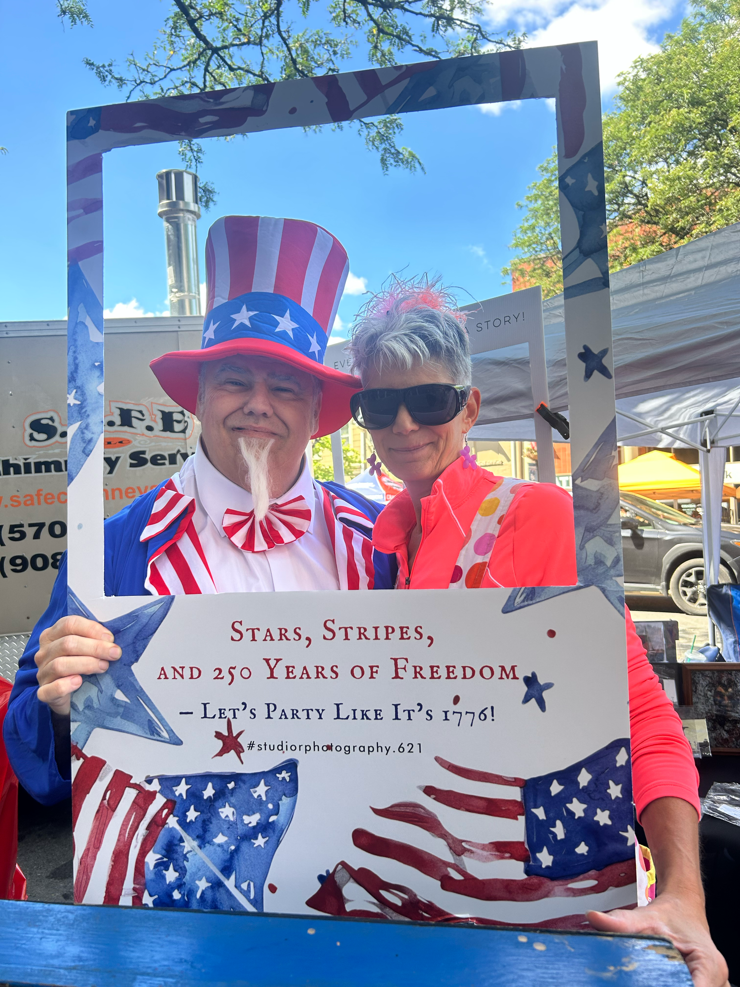 Patriotic banners and signs displaying stars and stripes themed messages at an outdoor Fourth of July celebration event.