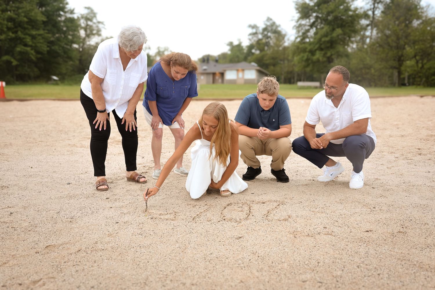 A group sits together on a sandy beach wearing casual white and navy blue clothing during a photo session.