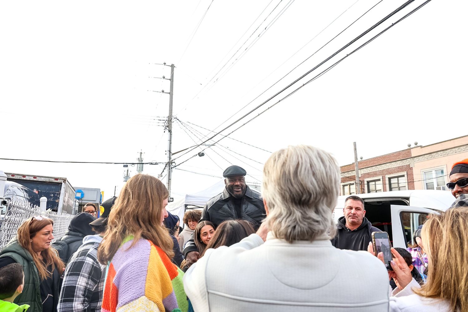 A group of people gather outdoors in a circle having a discussion near power lines and buildings.