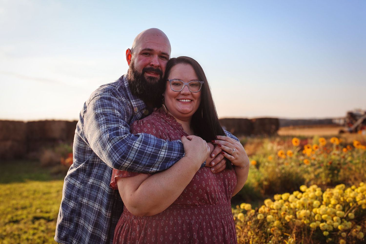 Couple embraces lovingly in a golden field of flowers during sunset.