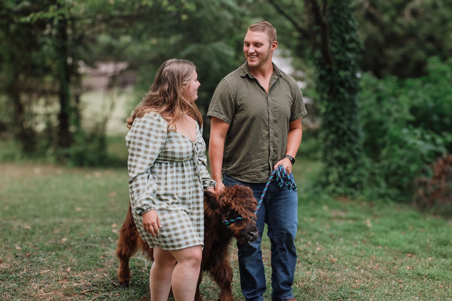 A couple stands together outdoors in a grassy field with trees in the background during a photo session.