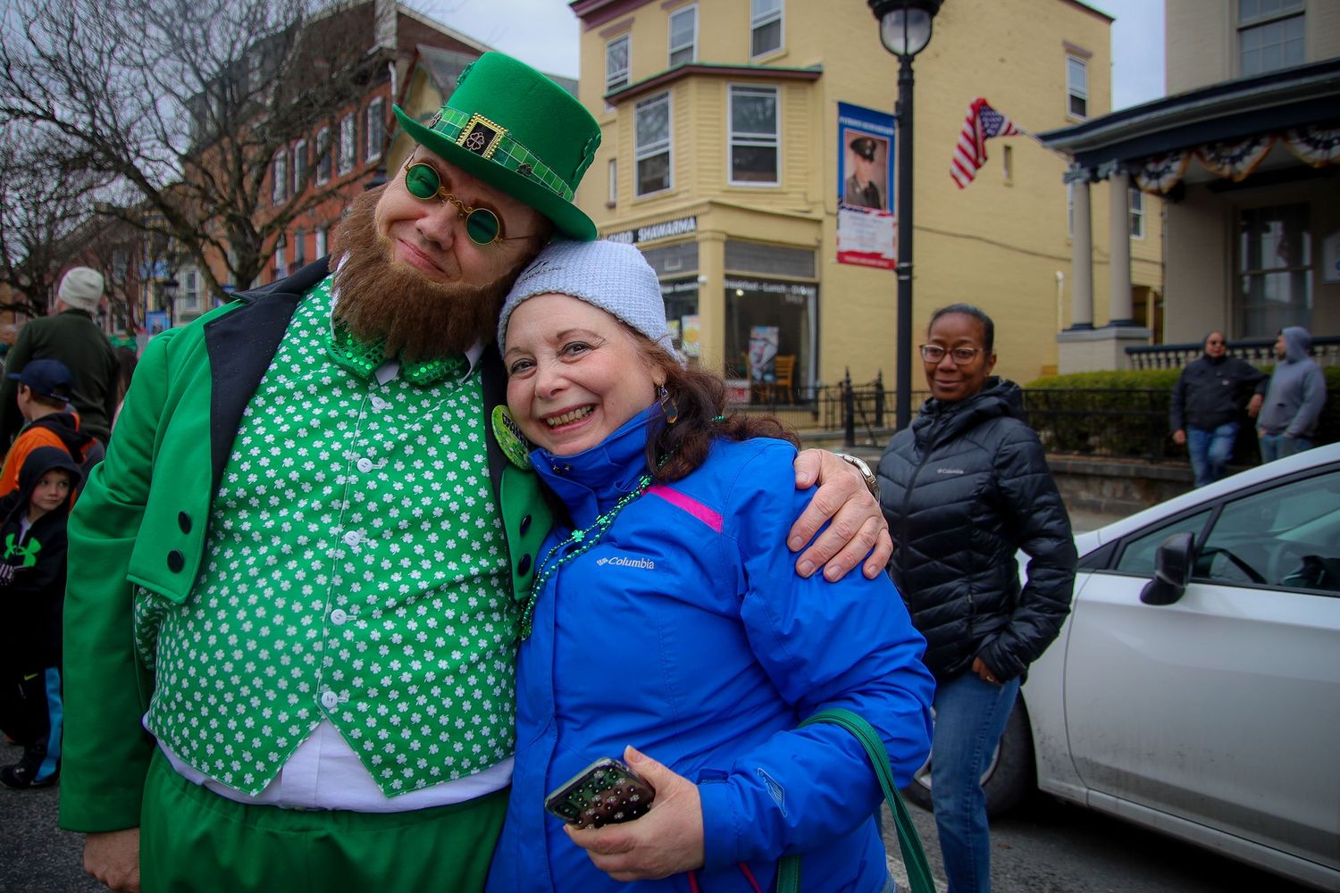 Two people celebrate at a St. Patrick's Day parade, one wearing a festive green outfit and the other in a blue winter coat.